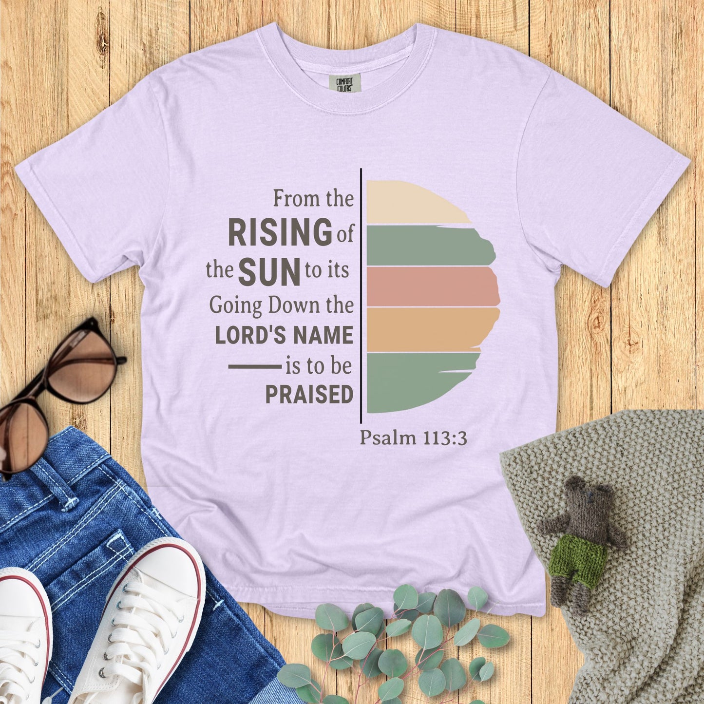 Purple t-shirt with sunset design and text on a wooden surface with accessories.