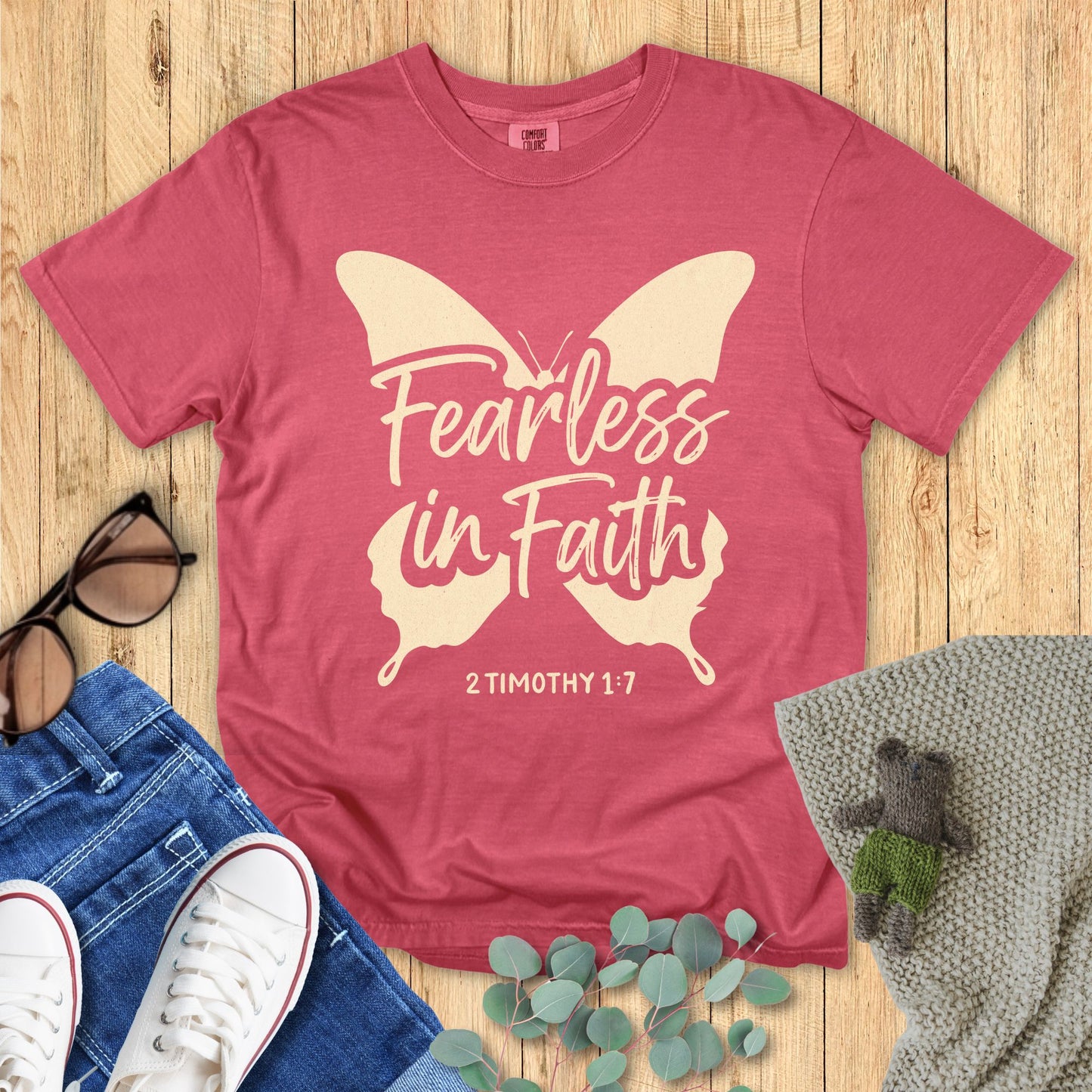 Crimson Red t-shirt with Butterfly 'Fearless in Faith' design on a wooden surface with accessories.