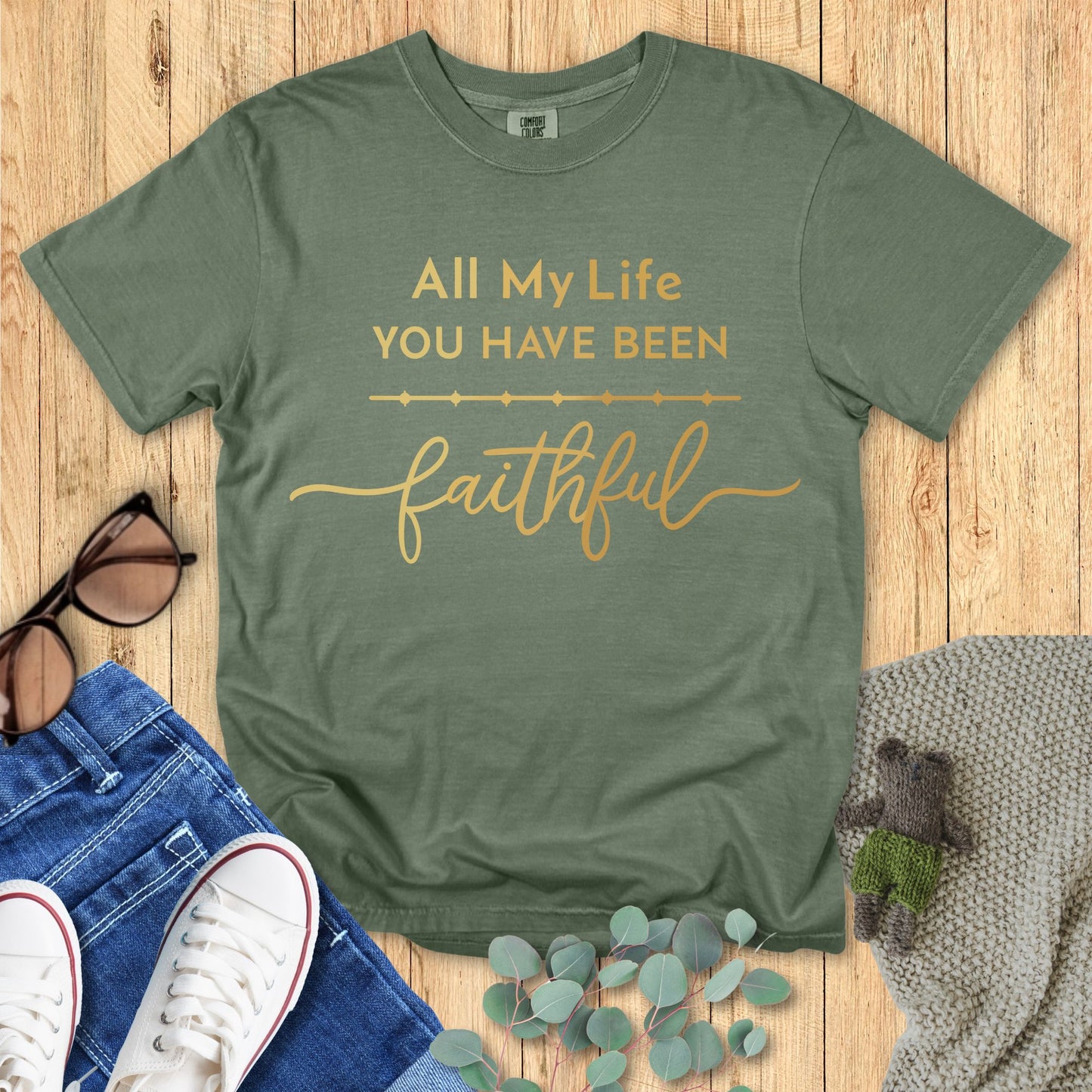 Green t-shirt with 'All My Life You Have Been Faithful' text on a wooden surface with accessories.