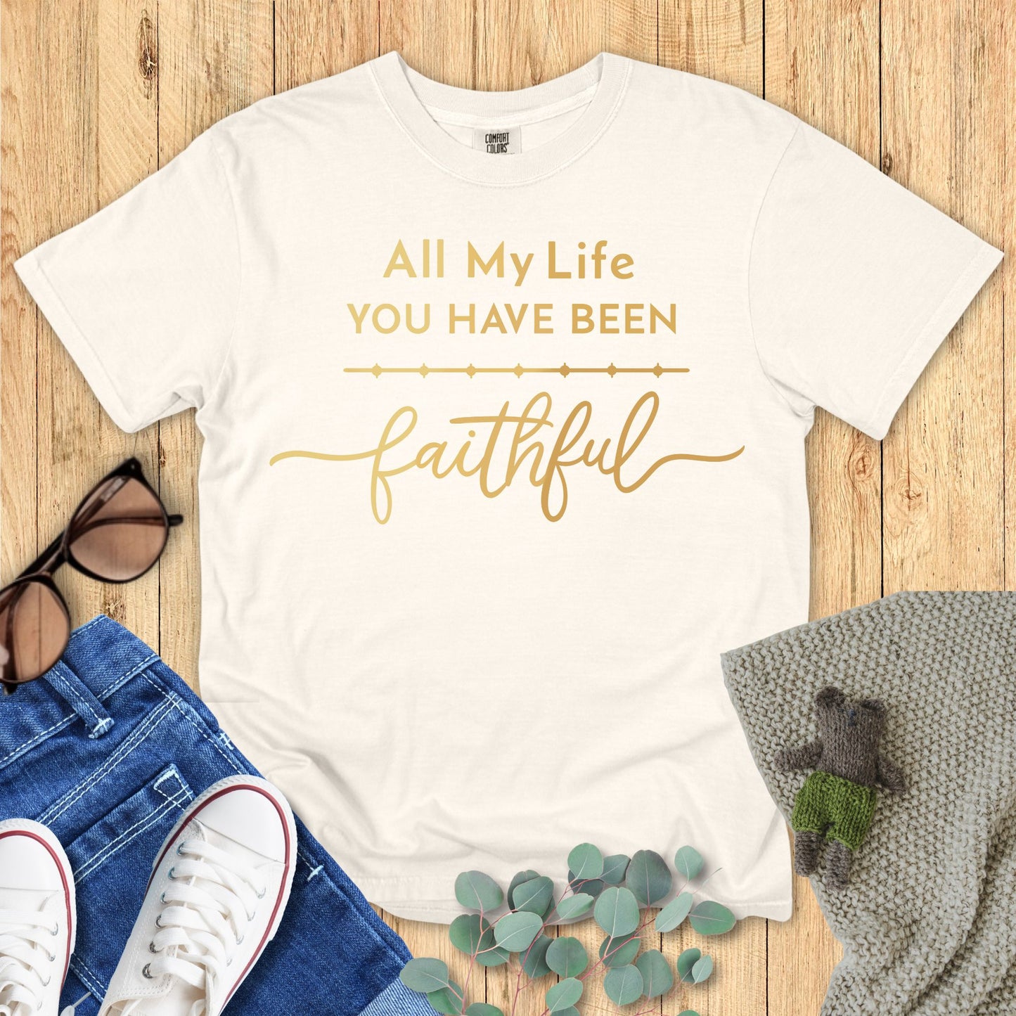 Ivory White t-shirt with gold text 'All My Life You Have Been Faithful' on a wooden surface with accessories.