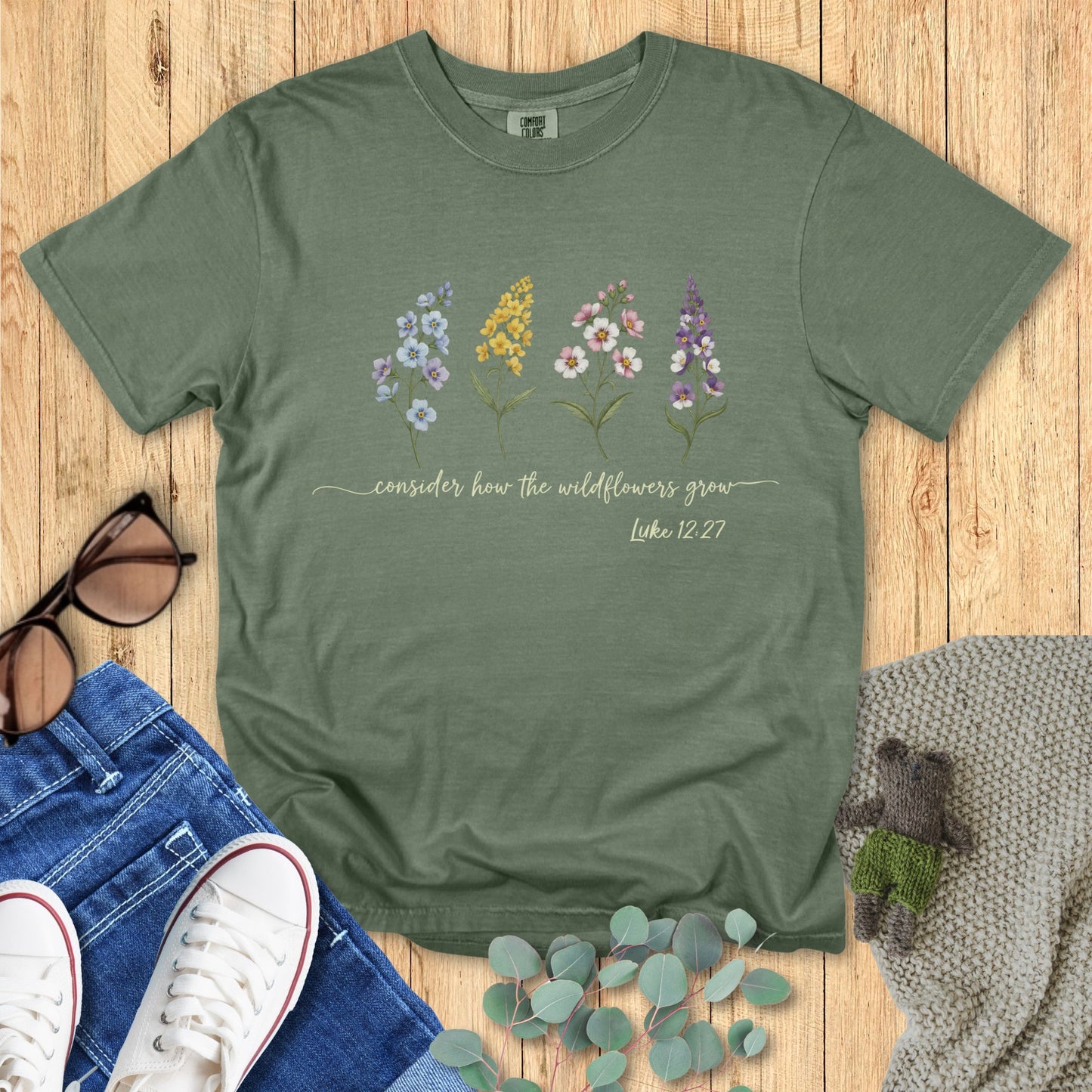 Green t-shirt with floral design and text on a wooden surface with accessories.