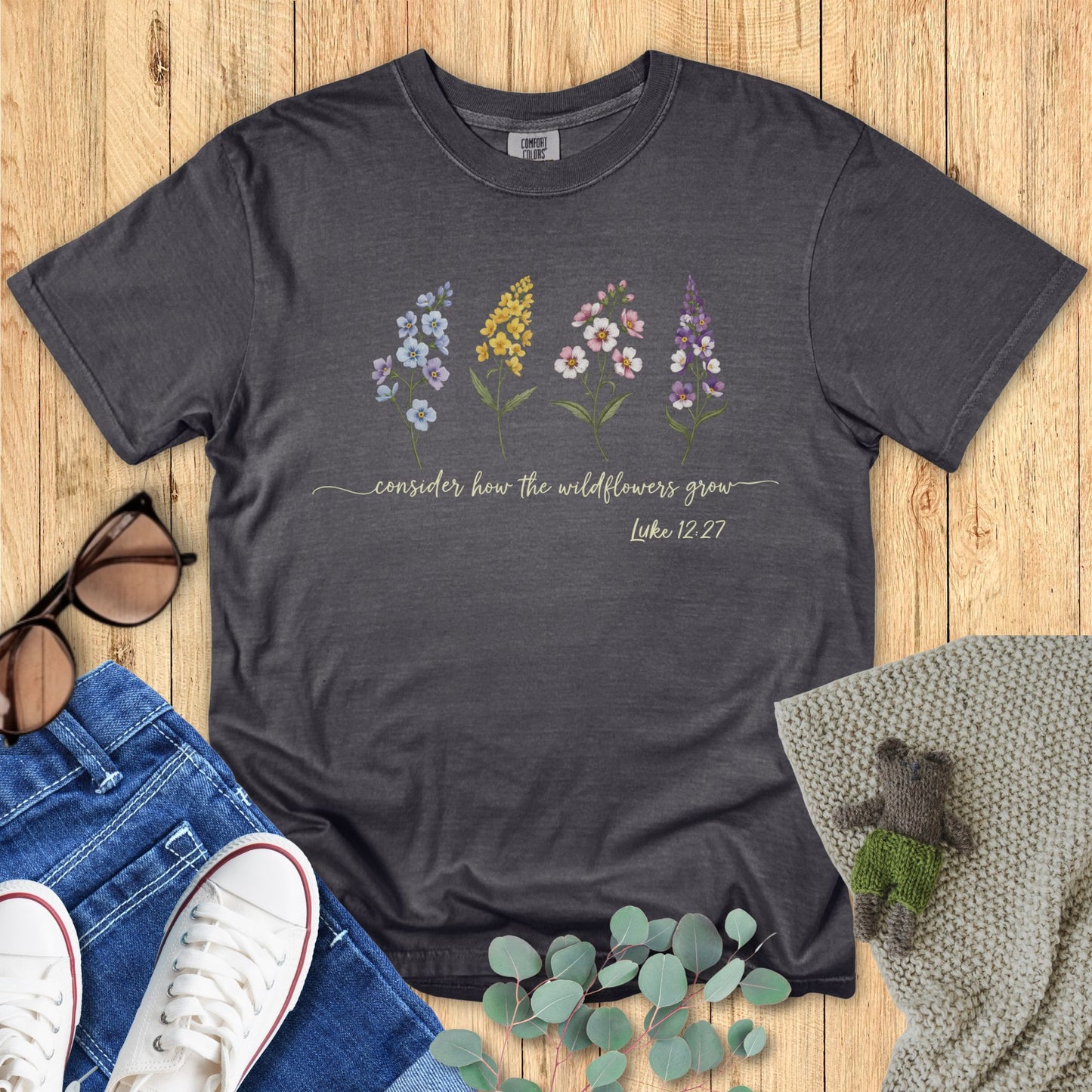 Dark gray t-shirt with floral design and text on a wooden surface with accessories.