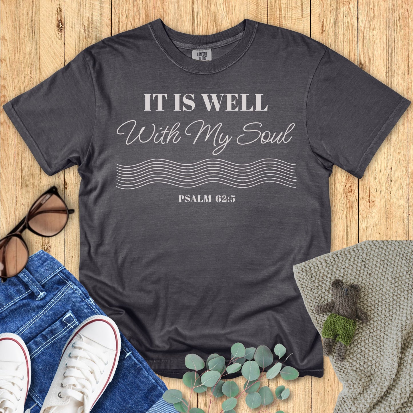 Dark gray t-shirt with 'It is Well with My Soul' text on a wooden surface with accessories.