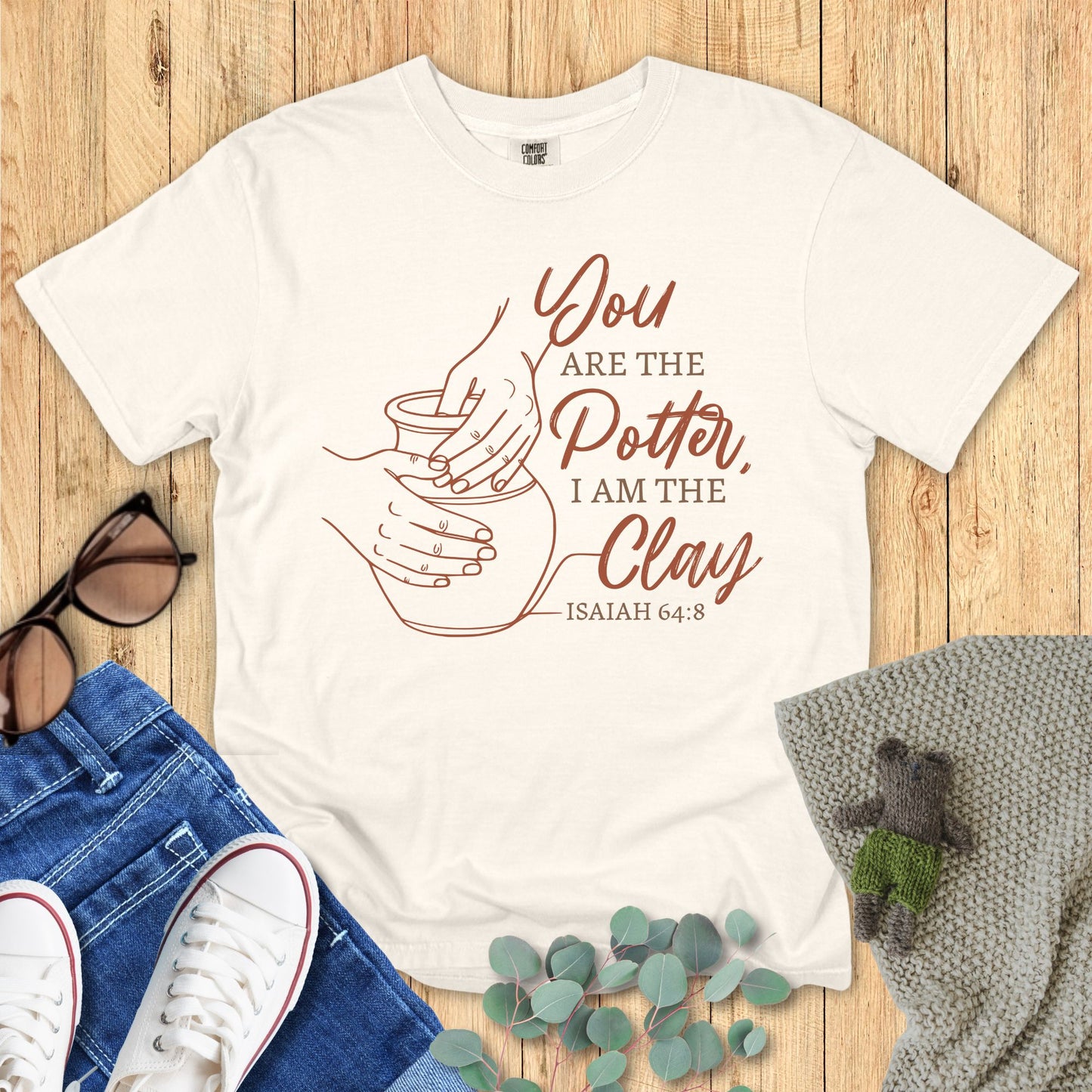 Ivory White t-shirt with 'You are the Potter, I am the Clay' design on a wooden surface with accessories.
