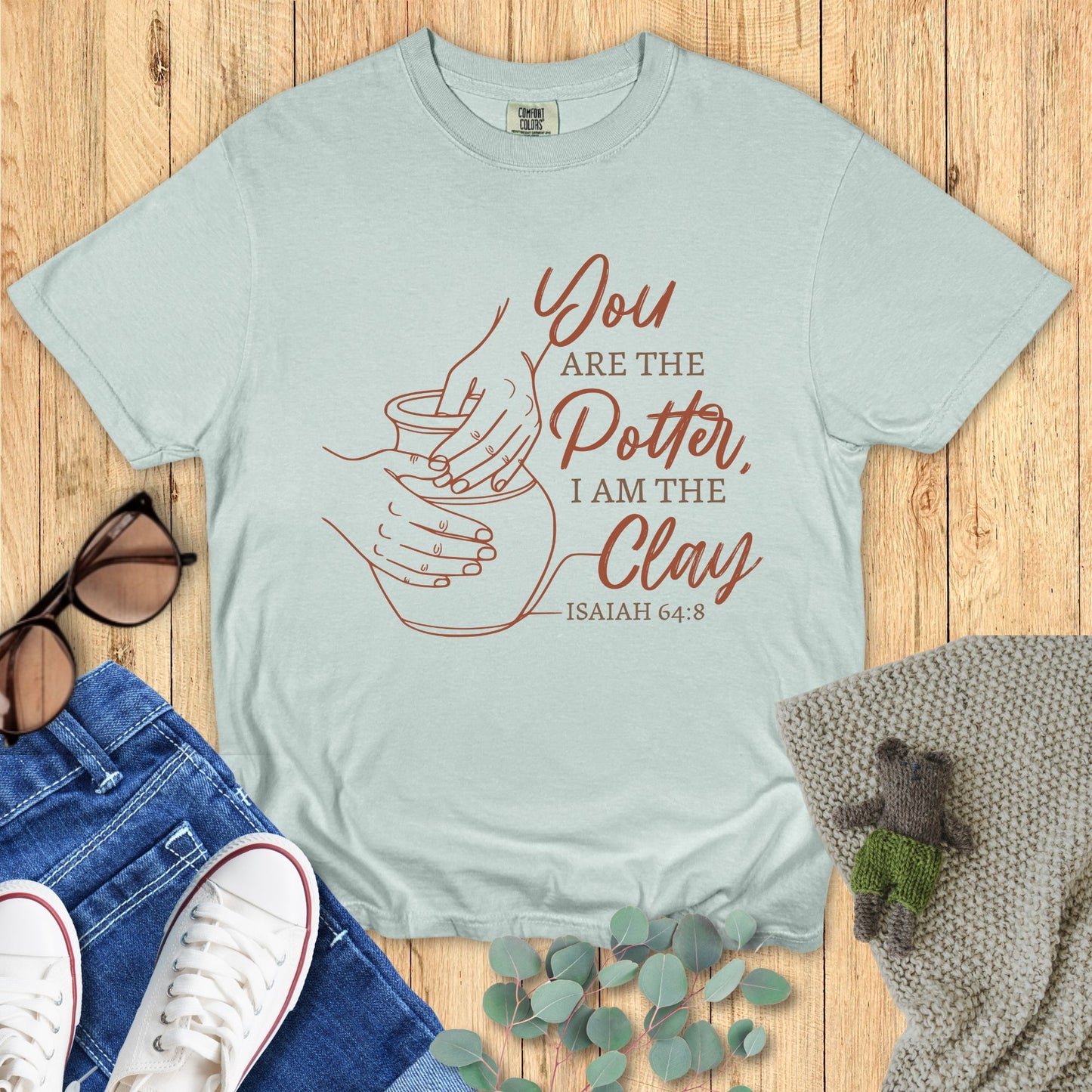 Light sage t-shirt with terracotta line art of hands shaping pottery and the words “You are the Potter, I am the Clay – Isaiah 64:8