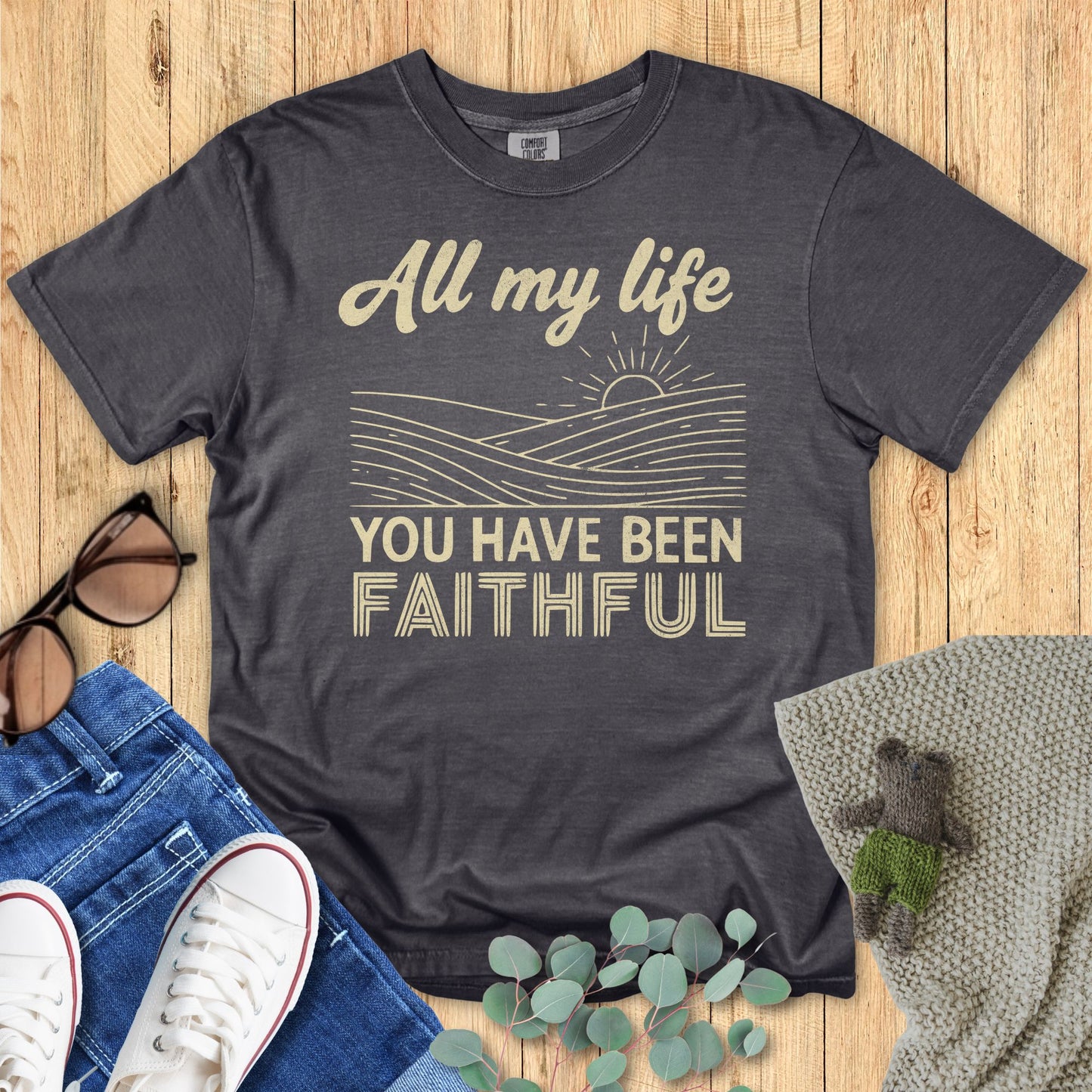 Gray t-shirt with motivational quote on a wooden surface with accessories.