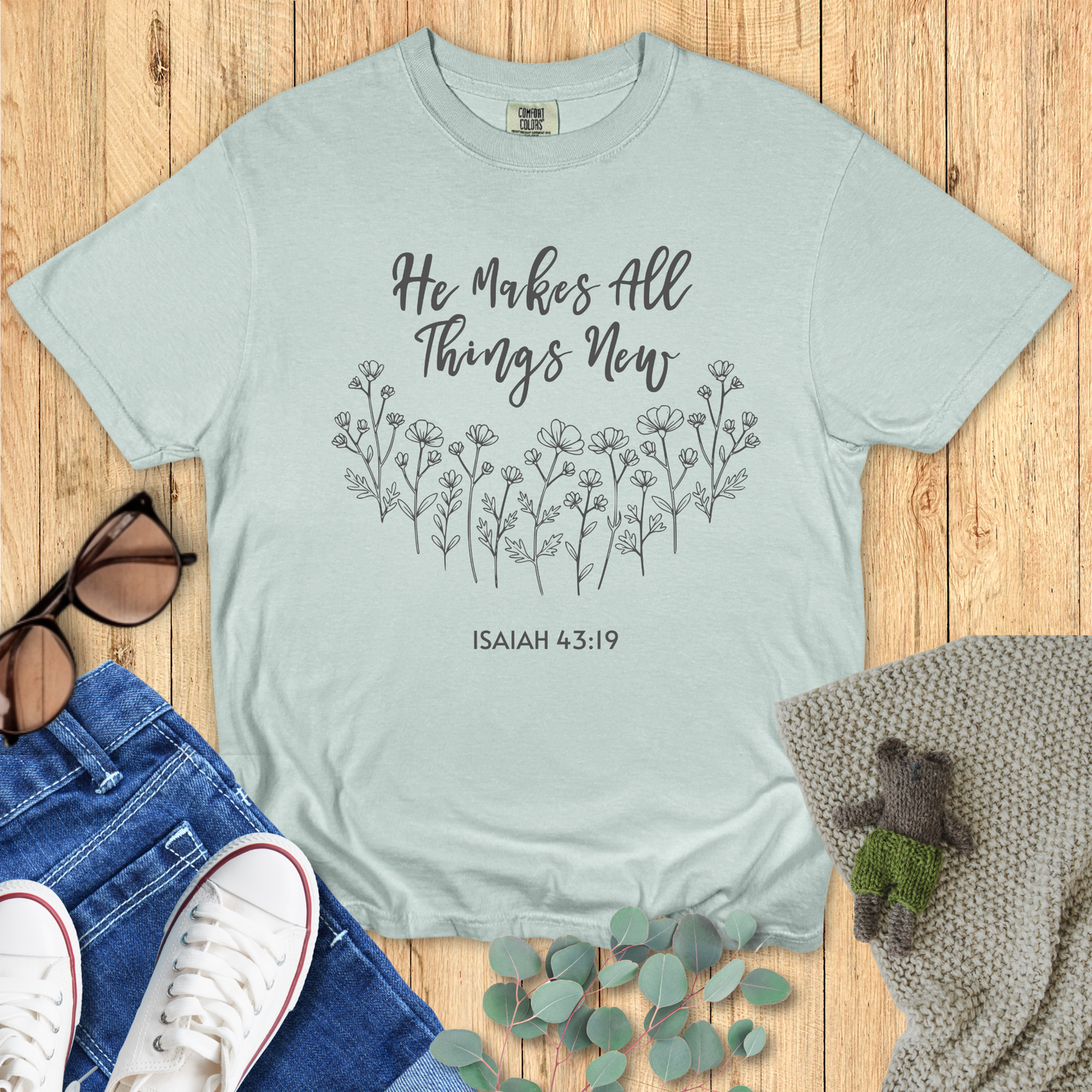 Light green t-shirt with hand-drawn floral design and the words “He Makes All Things New – Isaiah 43:19” in script.