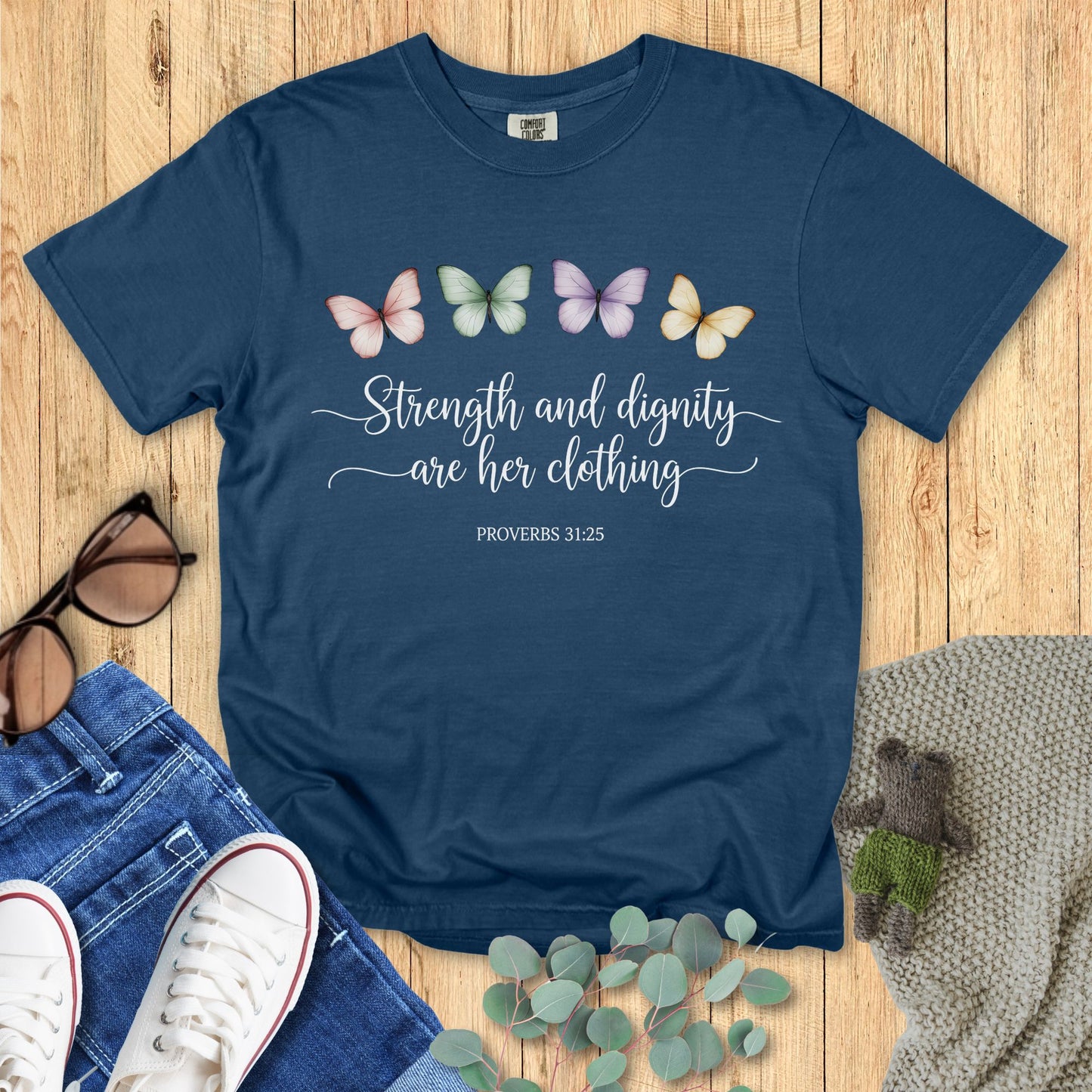 Blue t-shirt with butterfly design and text on a wooden surface with accessories.