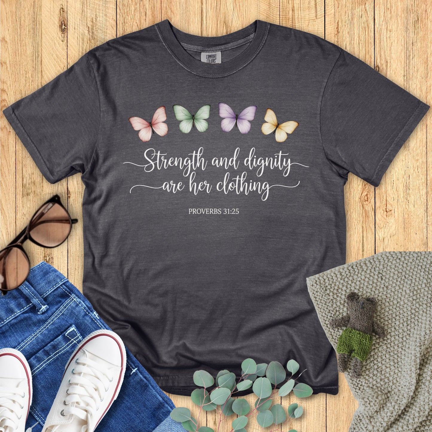 Dark gray t-shirt with butterfly design and text on a wooden surface with accessories.