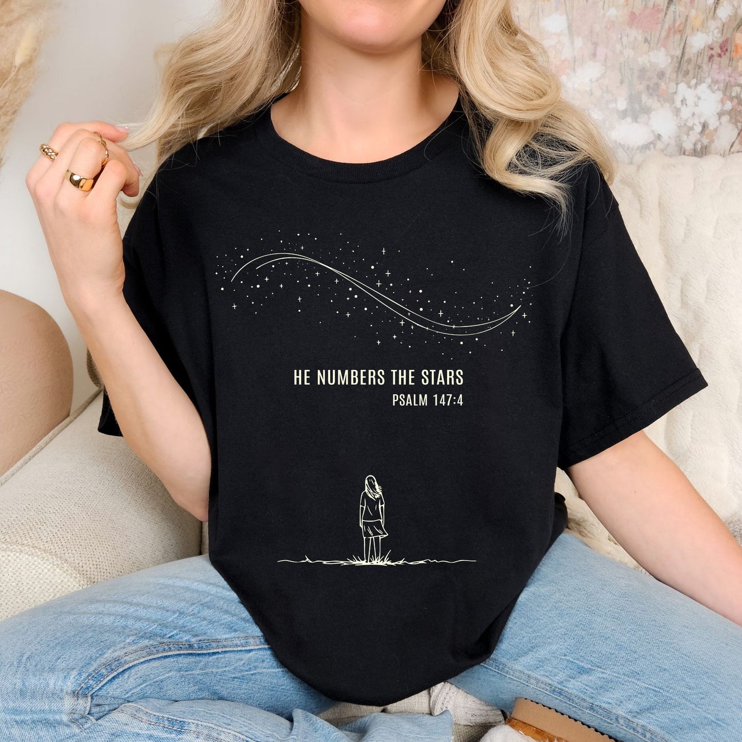 Person wearing a black T-shirt with a celestial design featuring a woman looking up at a sky full of stars, with the words “He Numbers the Stars – Psalm 147:4” printed below