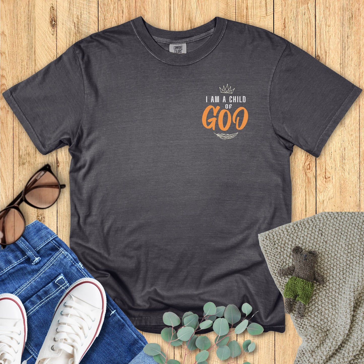 Dark gray t-shirt with 'I am a Child of Goo' text on a wooden surface with accessories.