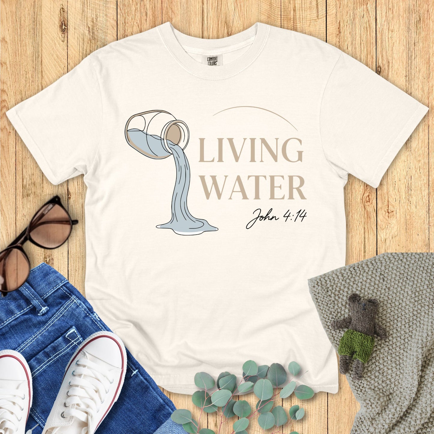 Ivory White t-shirt with 'Living Water' design and text on a wooden surface with accessories.