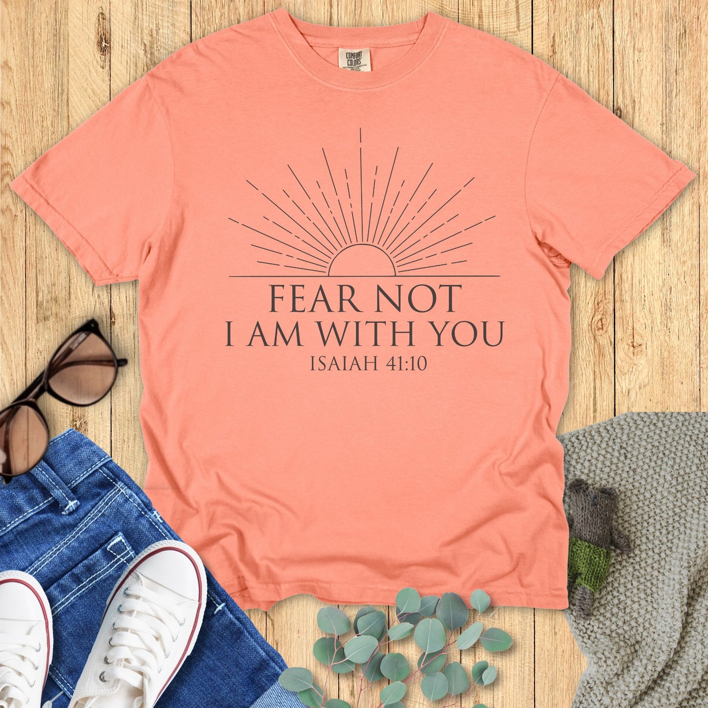 Coral t-shirt with 'Fear Not, I am with you' text on a wooden surface with accessories.