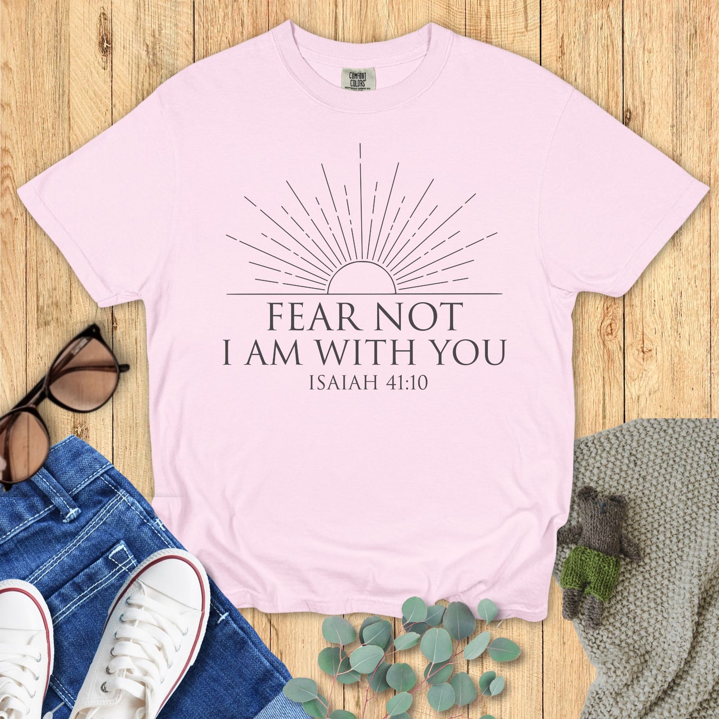 Pink t-shirt with 'Fear Not, I am with you' text on a wooden surface with accessories.