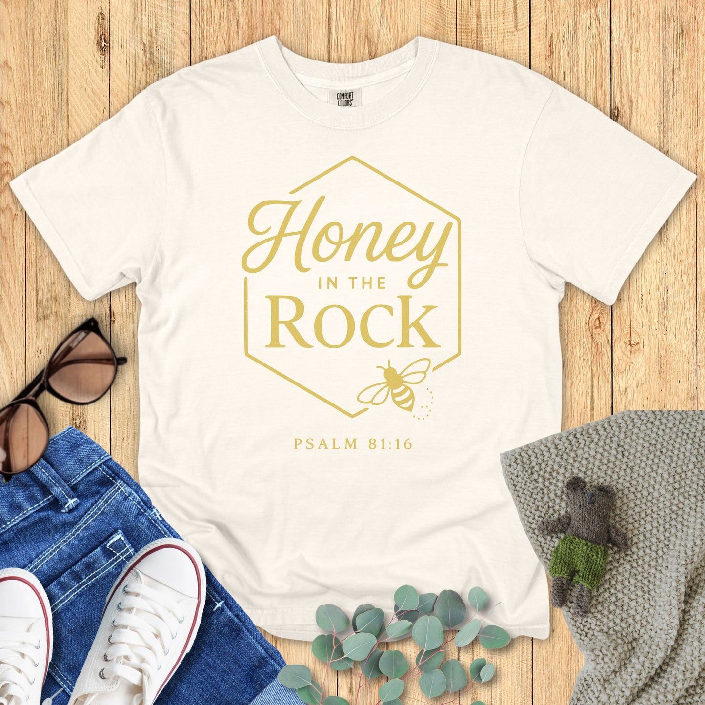 Ivory White t-shirt with 'Honey in the Rock' text on a wooden surface with accessories.