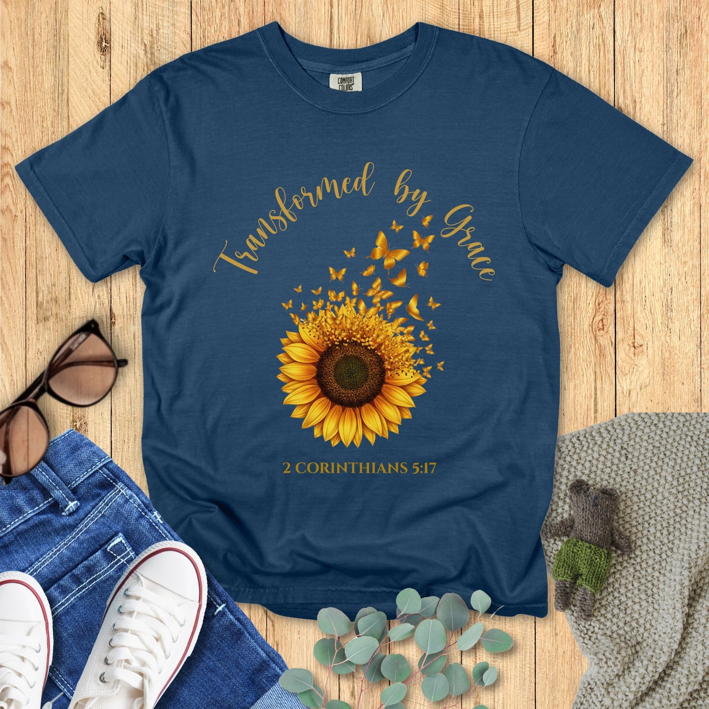 Blue t-shirt with sunflower design and text on a wooden surface with accessories.