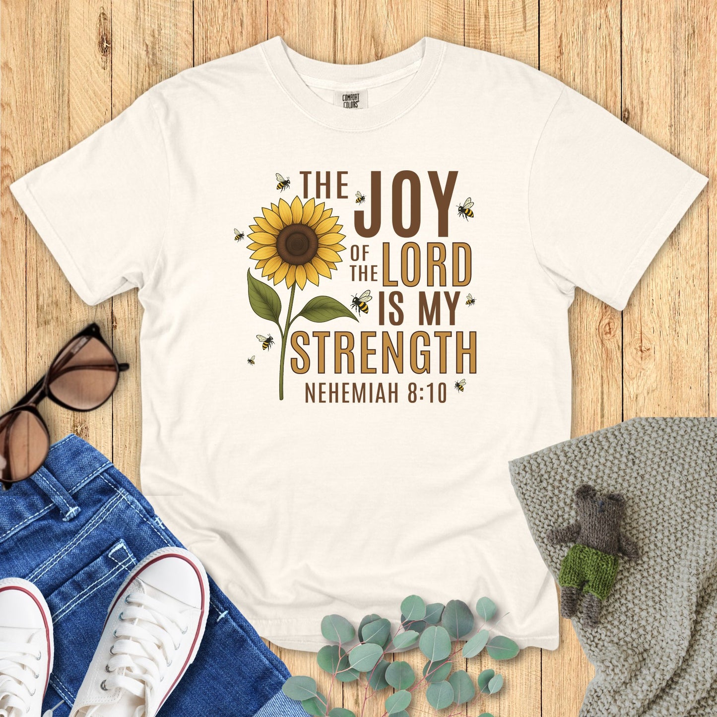 Ivory White t-shirt with sunflower design and text on a wooden surface with accessories.