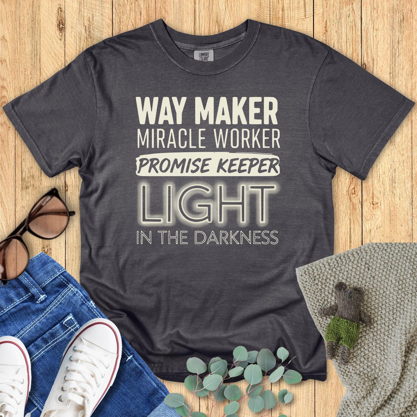 Gray t-shirt with motivational text on a wooden surface with accessories.