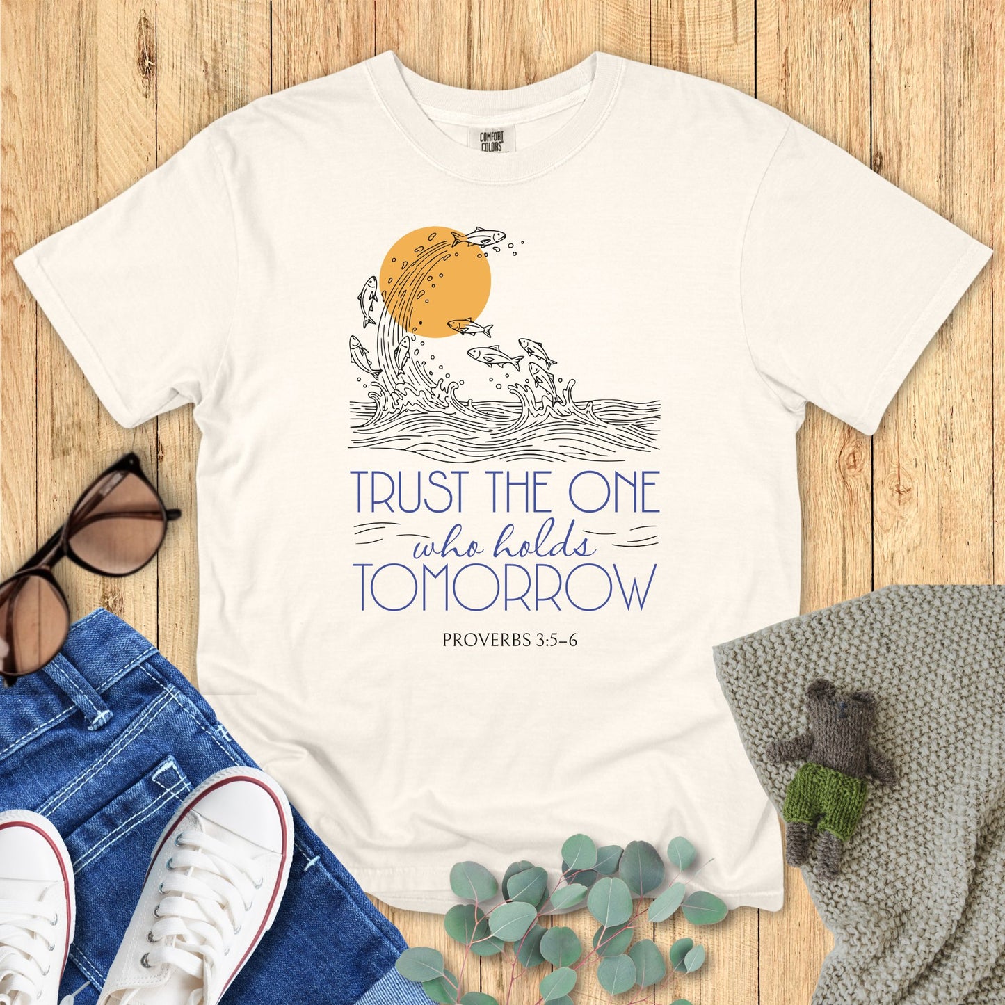 Ivory White t-shirt with motivational quote and design on a wooden surface with accessories.