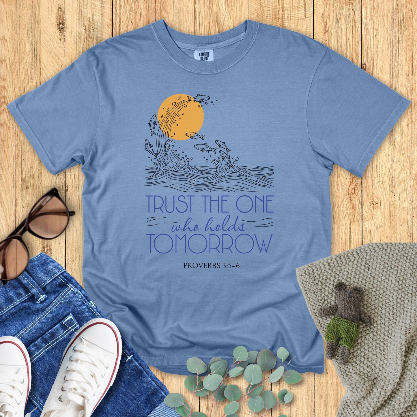 Blue t-shirt with motivational design on a wooden surface with accessories.
