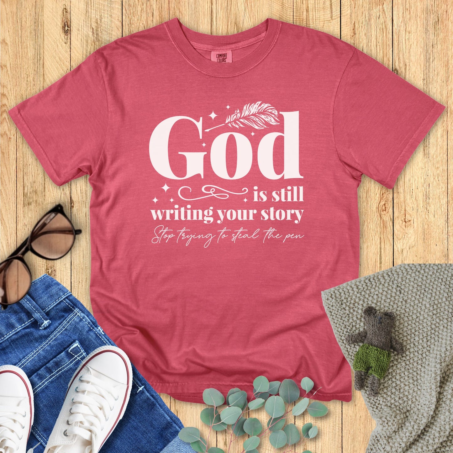 crimson Red t-shirt with motivational quote on a wooden surface with accessories.