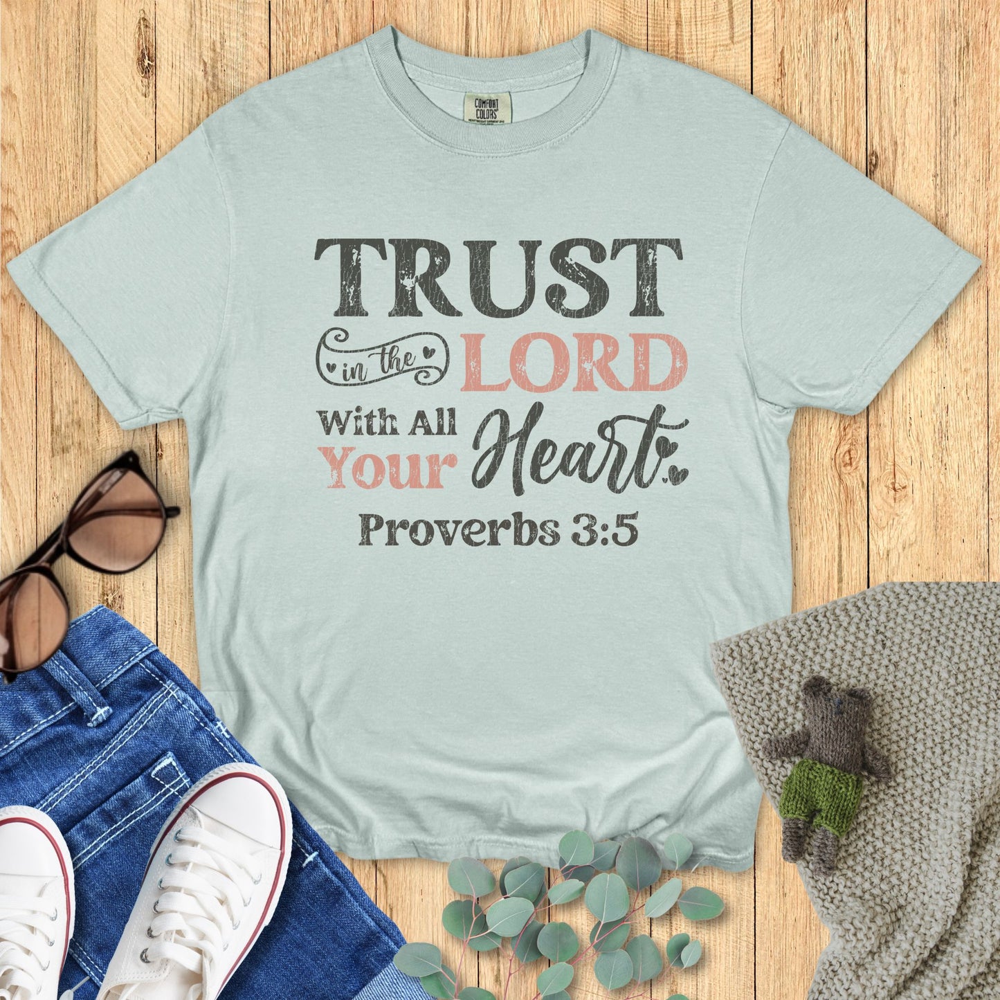 Light blue t-shirt with motivational quote on a wooden surface with accessories.