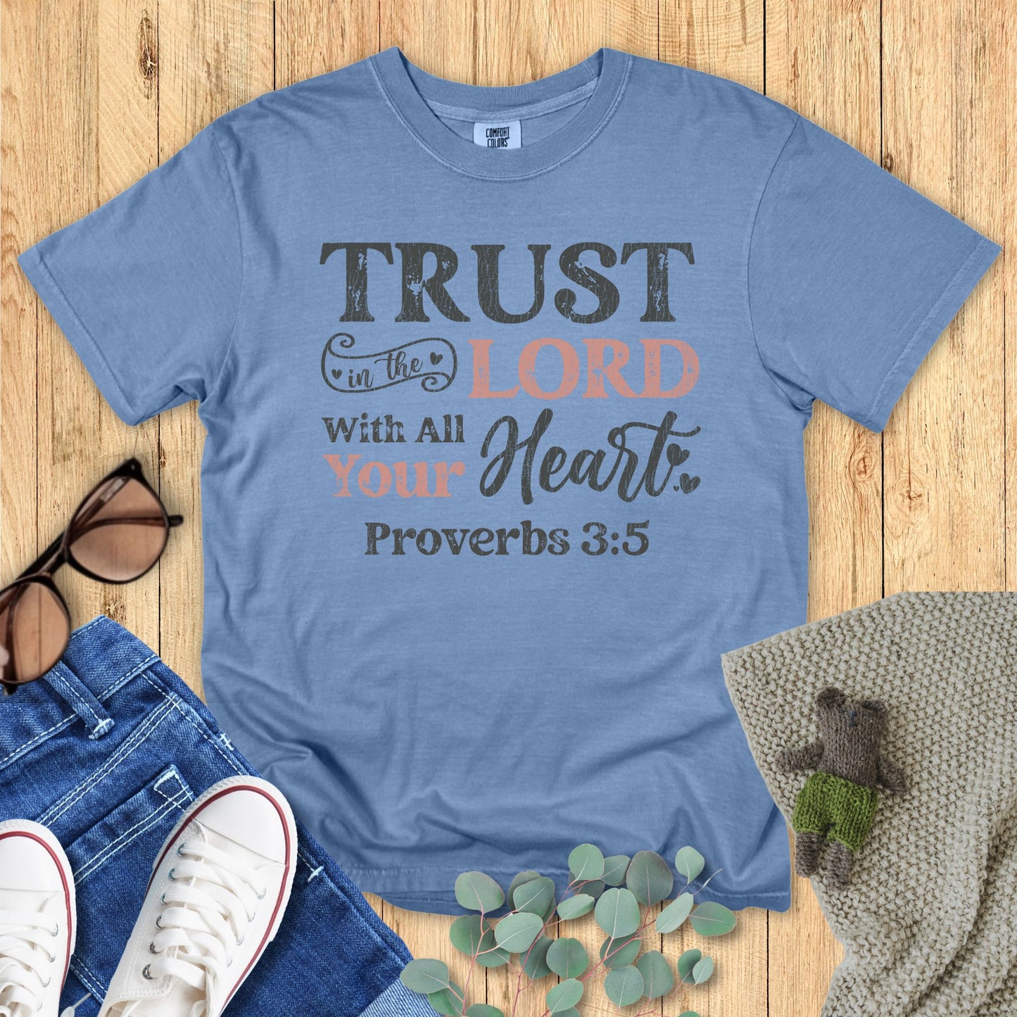 Blue t-shirt with motivational quote on a wooden surface with accessories.