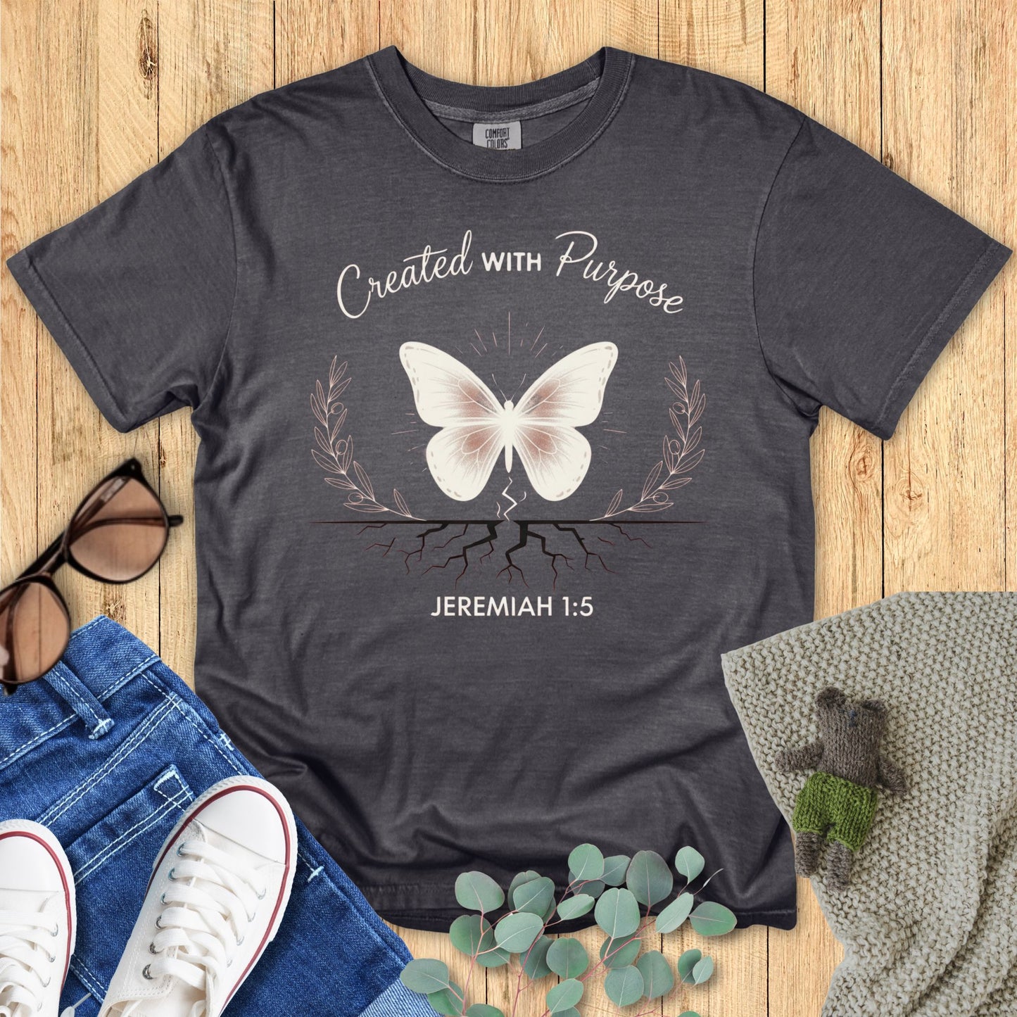 Dark gray t-shirt with butterfly graphic and 'Created with Purpose' text on a wooden surface.