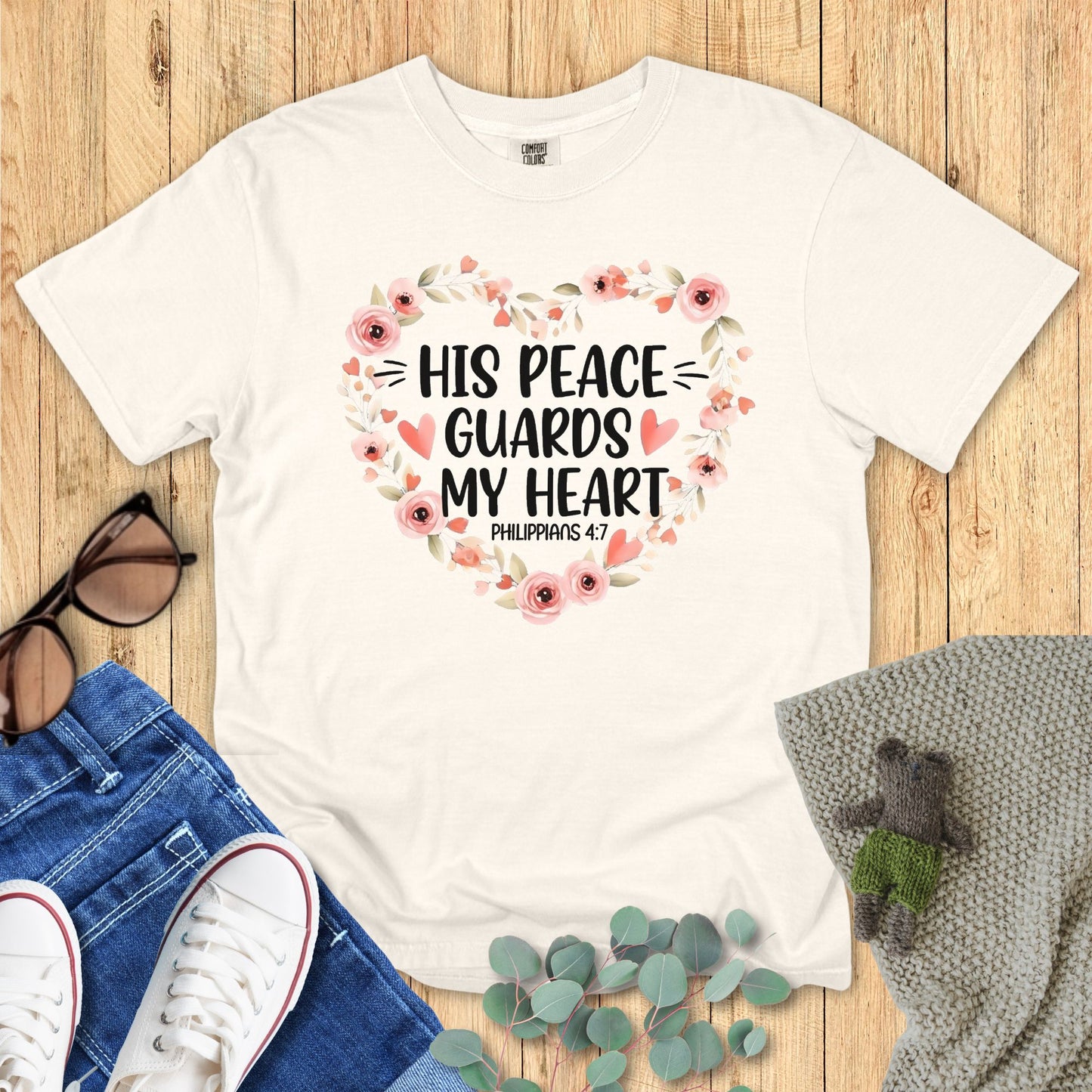 White t-shirt with floral design and text on a wooden surface with accessories.
