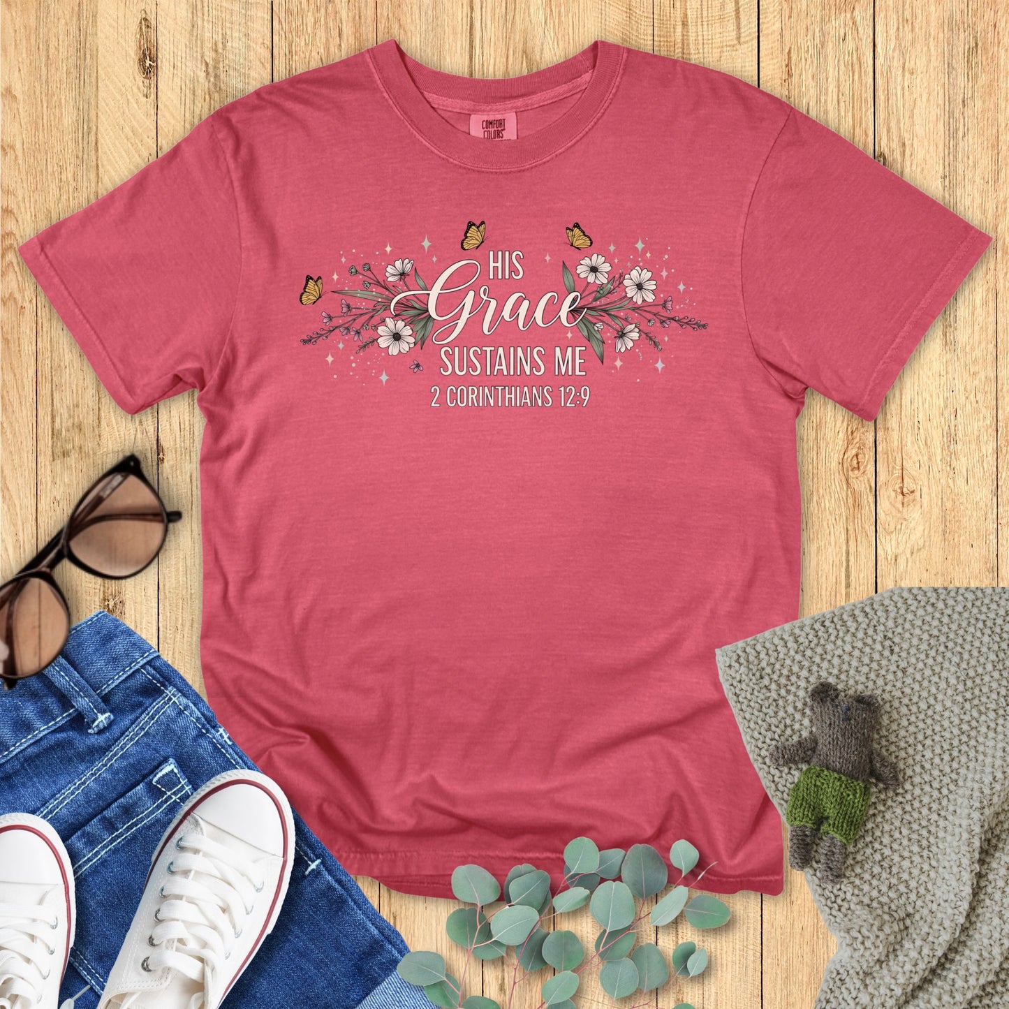 Crimson red t-shirt with floral design and text on a wooden surface with accessories.