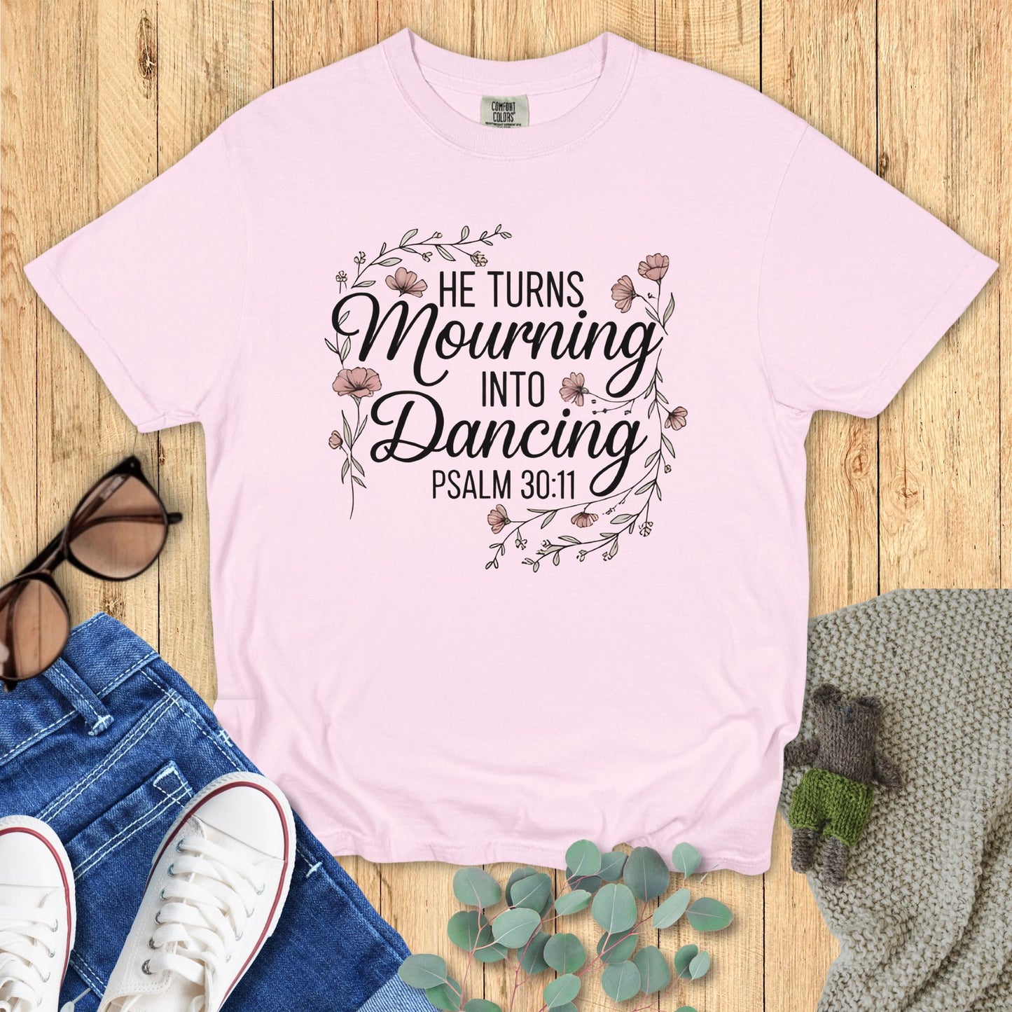 Pink t-shirt with motivational quote on a wooden surface with accessories.
