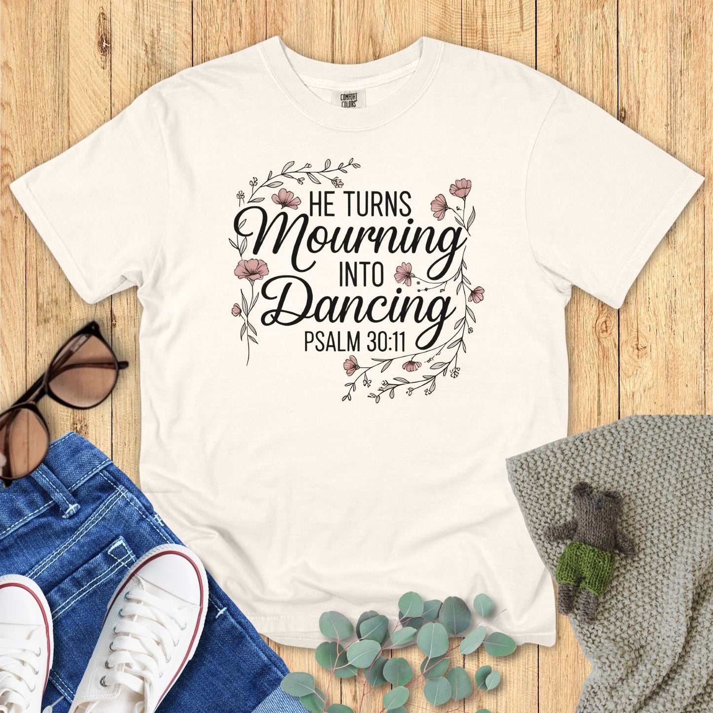 White t-shirt with motivational quote on a wooden surface with accessories.
