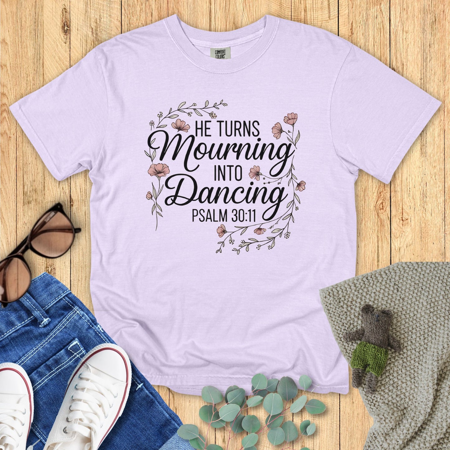 Light purple t-shirt with motivational quote on a wooden surface with accessories.
