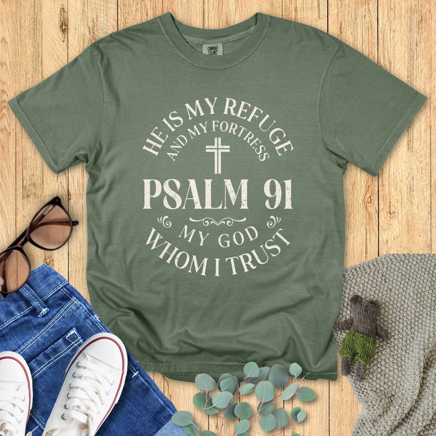 Green t-shirt with Psalm 91 text on a wooden surface with accessories.