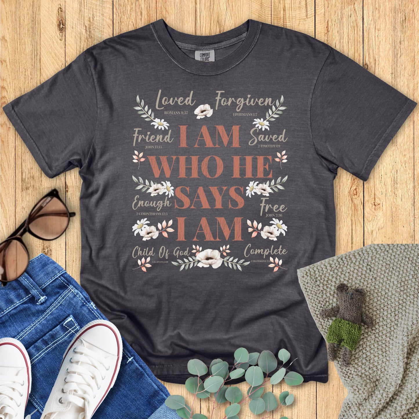 Dark gray t-shirt with motivational text and floral designs on a wooden surface with accessories.