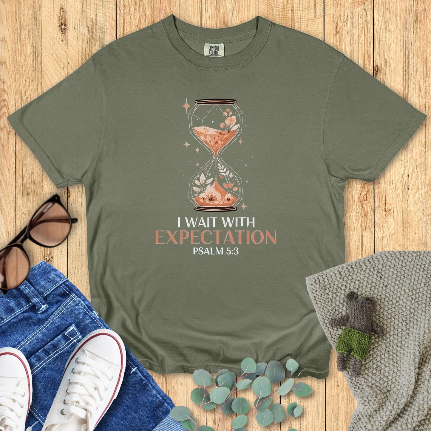 Green t-shirt with hourglass design and text on a wooden surface with accessories.