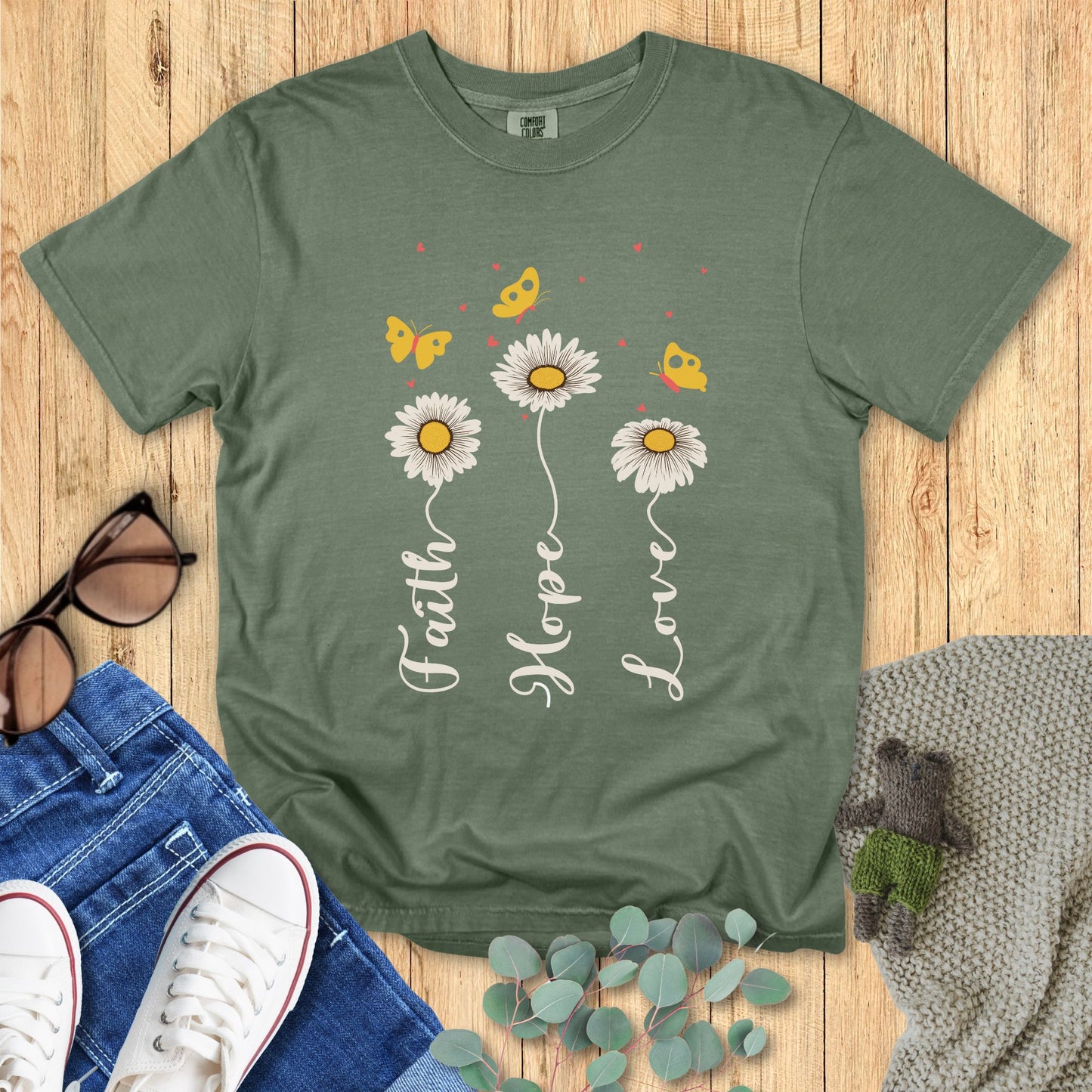 Green t-shirt with floral design and text on a wooden surface with accessories.