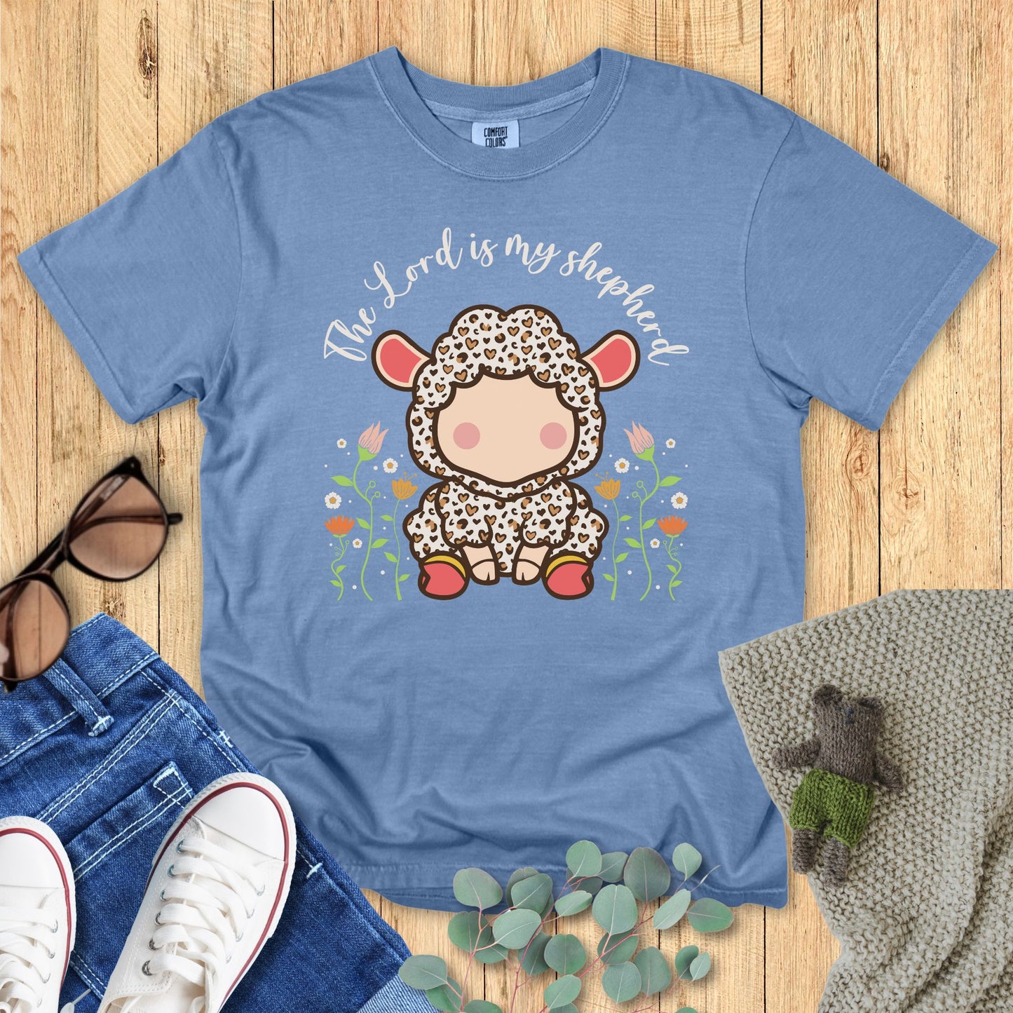 Blue t-shirt with a cartoon lamb design and 'The Lord is my shepherd' text on a wooden surface.