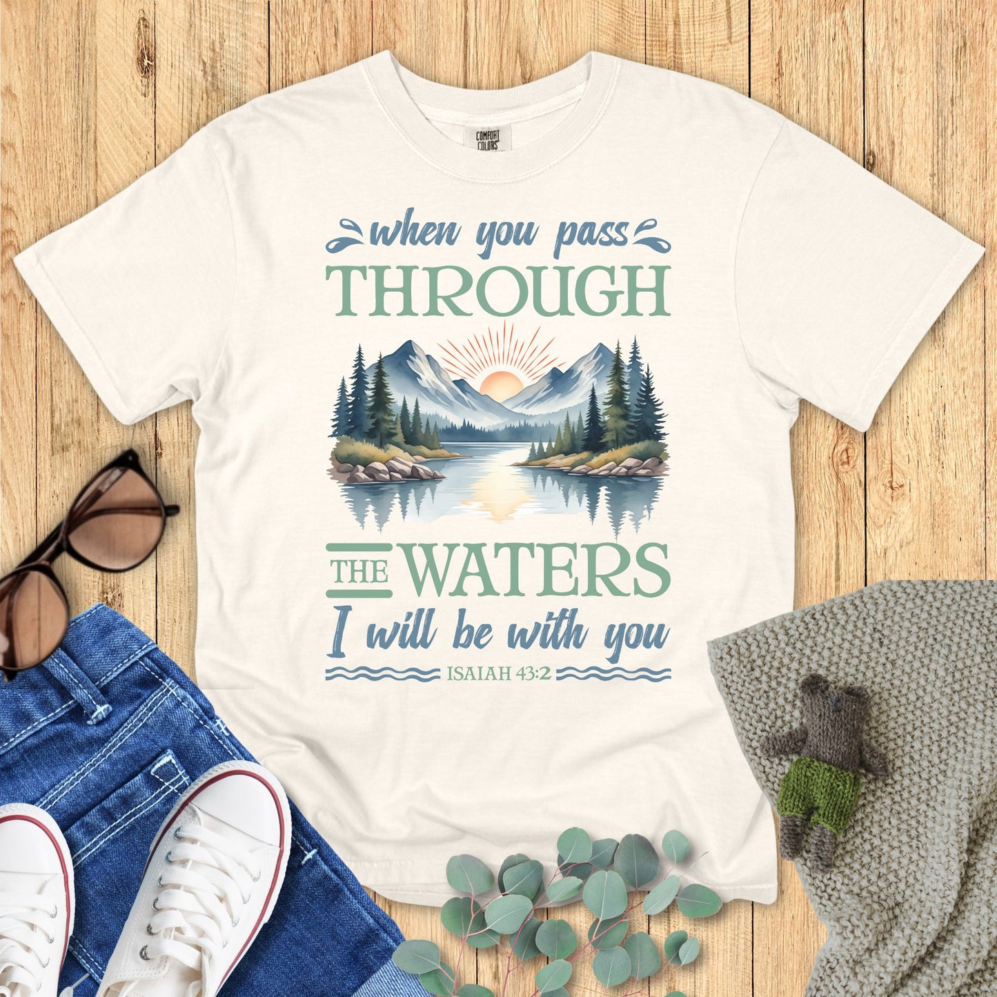 Ivory t-shirt with nature-themed design and text on a wooden surface with accessories.