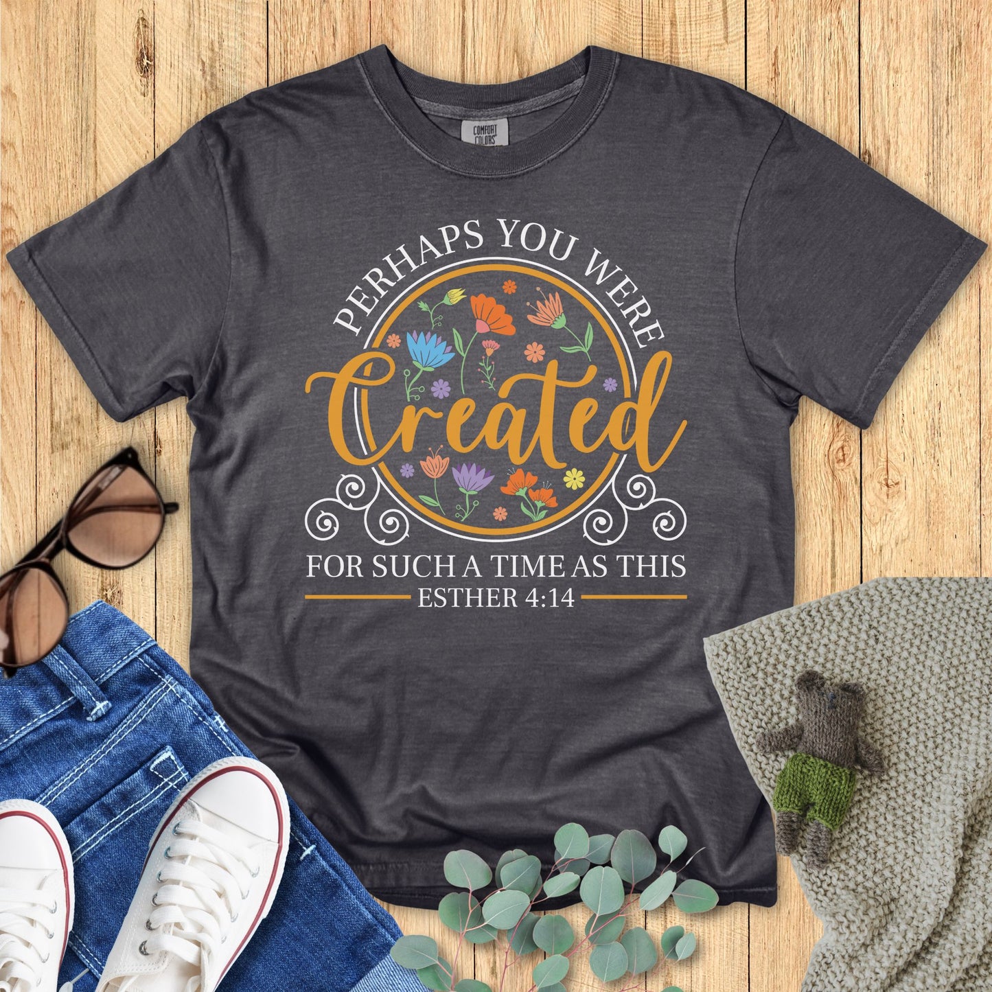 Dark gray t-shirt with floral design and text on a wooden surface with accessories.