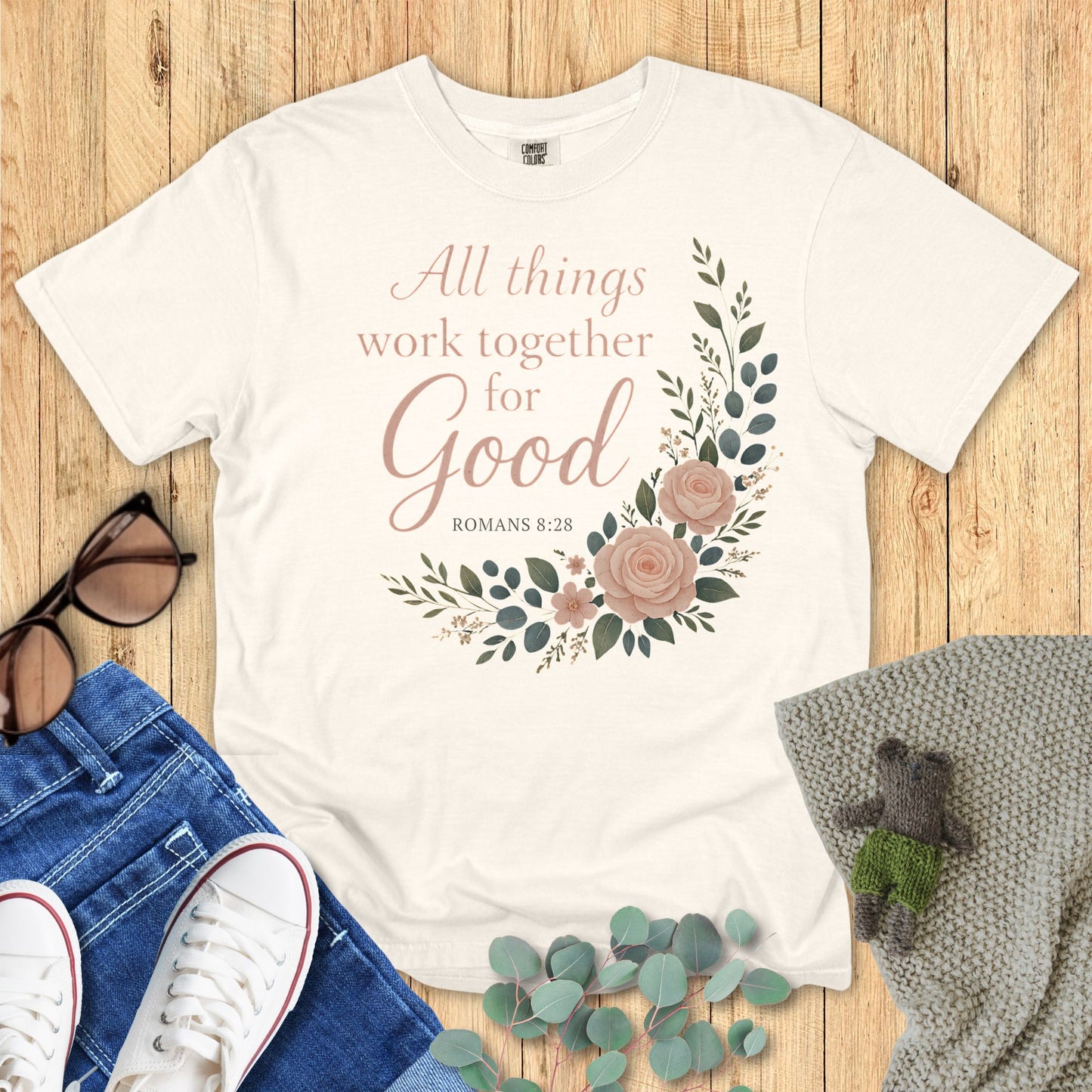 Ivory t-shirt with floral design and text on a wooden surface with accessories.
