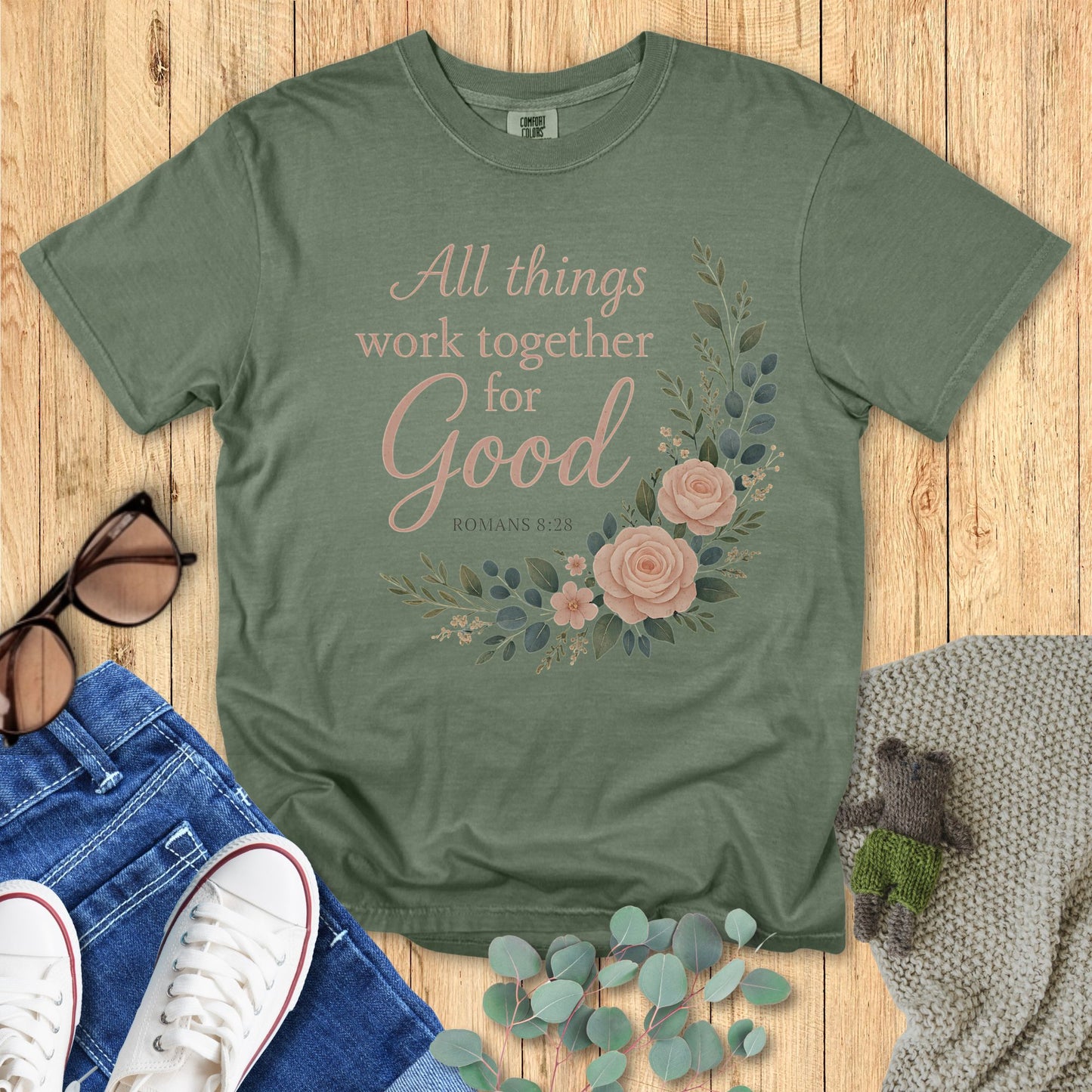Green t-shirt with floral design and text on a wooden surface with accessories.