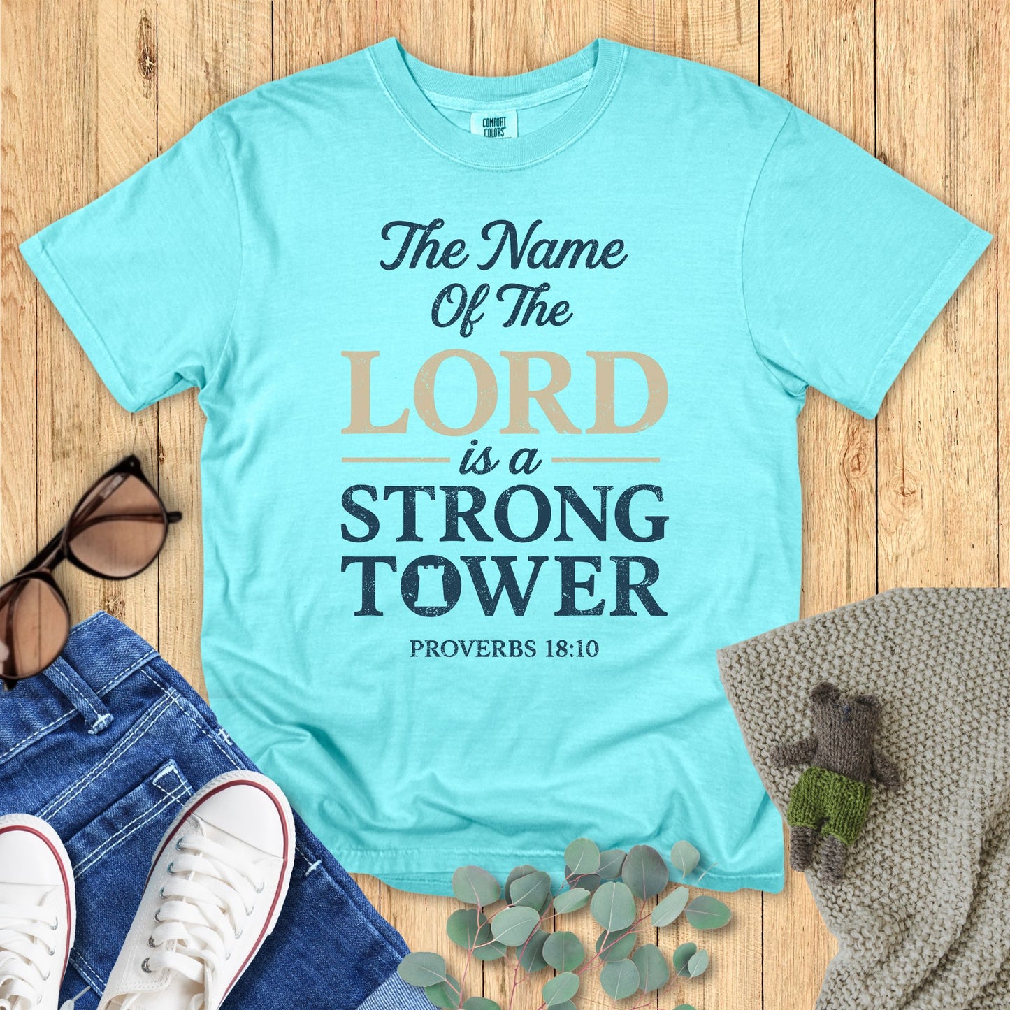 Light blue t-shirt with motivational quote on a wooden surface with accessories.