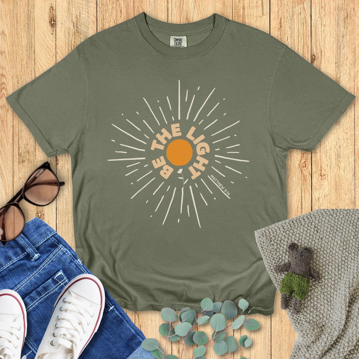 Green t-shirt with sun graphic and text on a wooden surface with accessories.