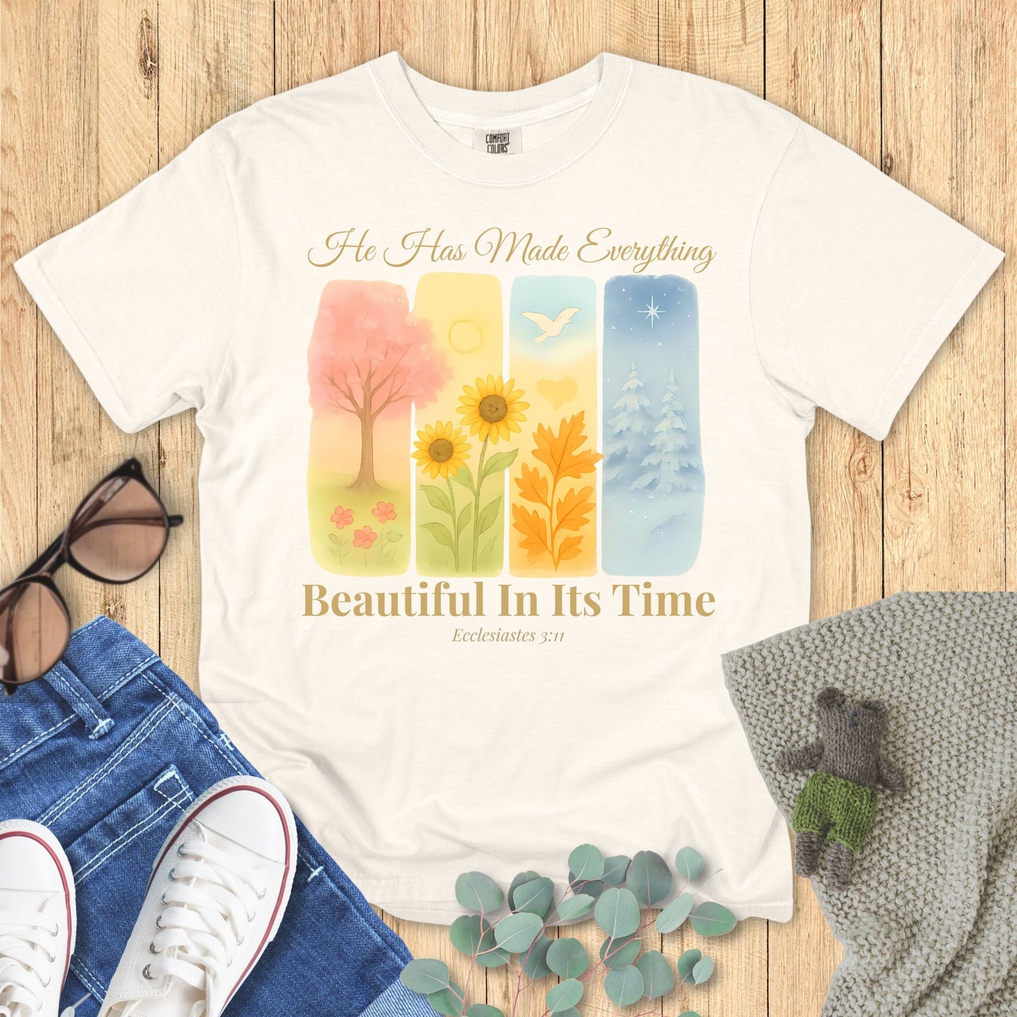 Ivory t-shirt with nature-themed design and inspirational quote on a wooden surface with accessories.