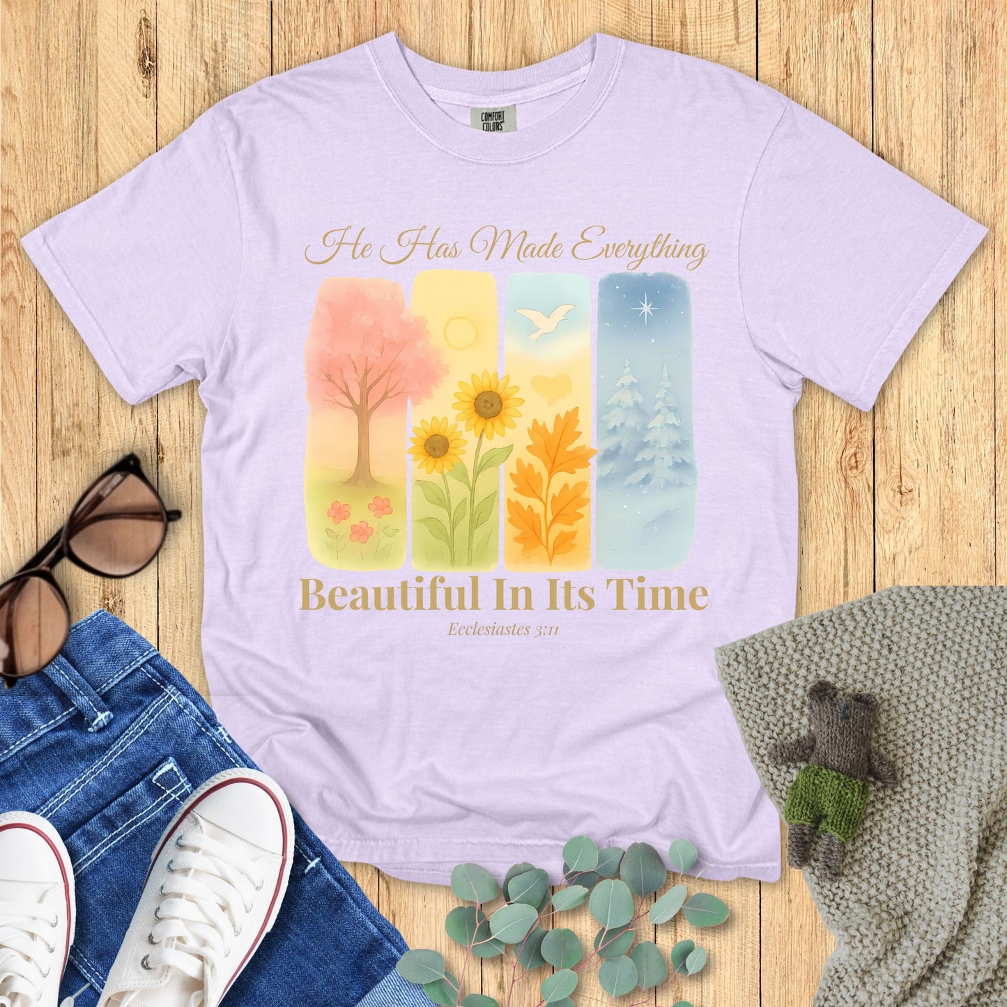 Lavender t-shirt with nature-themed design and text on a wooden surface with accessories.