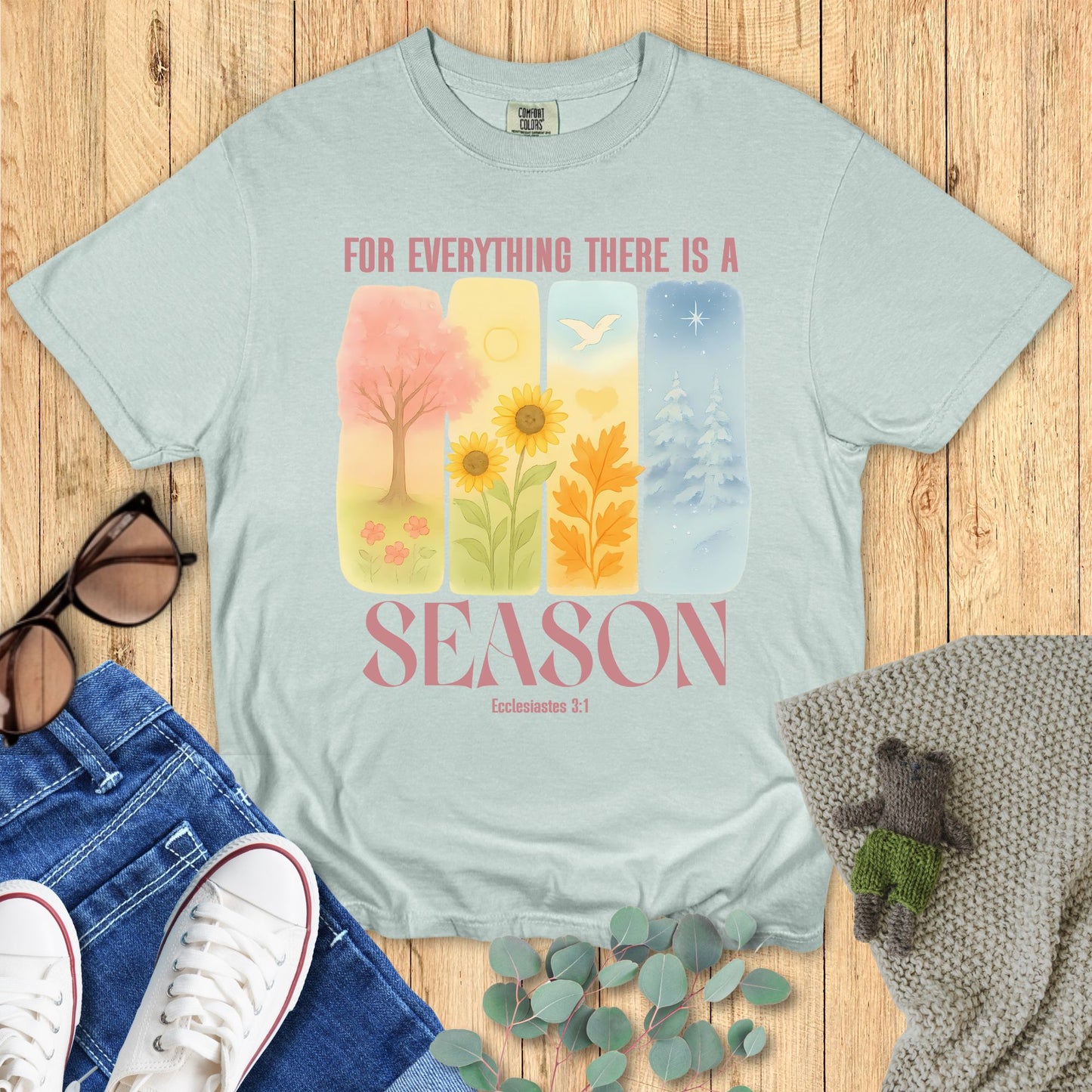 Light green t-shirt with nature-themed design and text on a wooden surface with accessories.