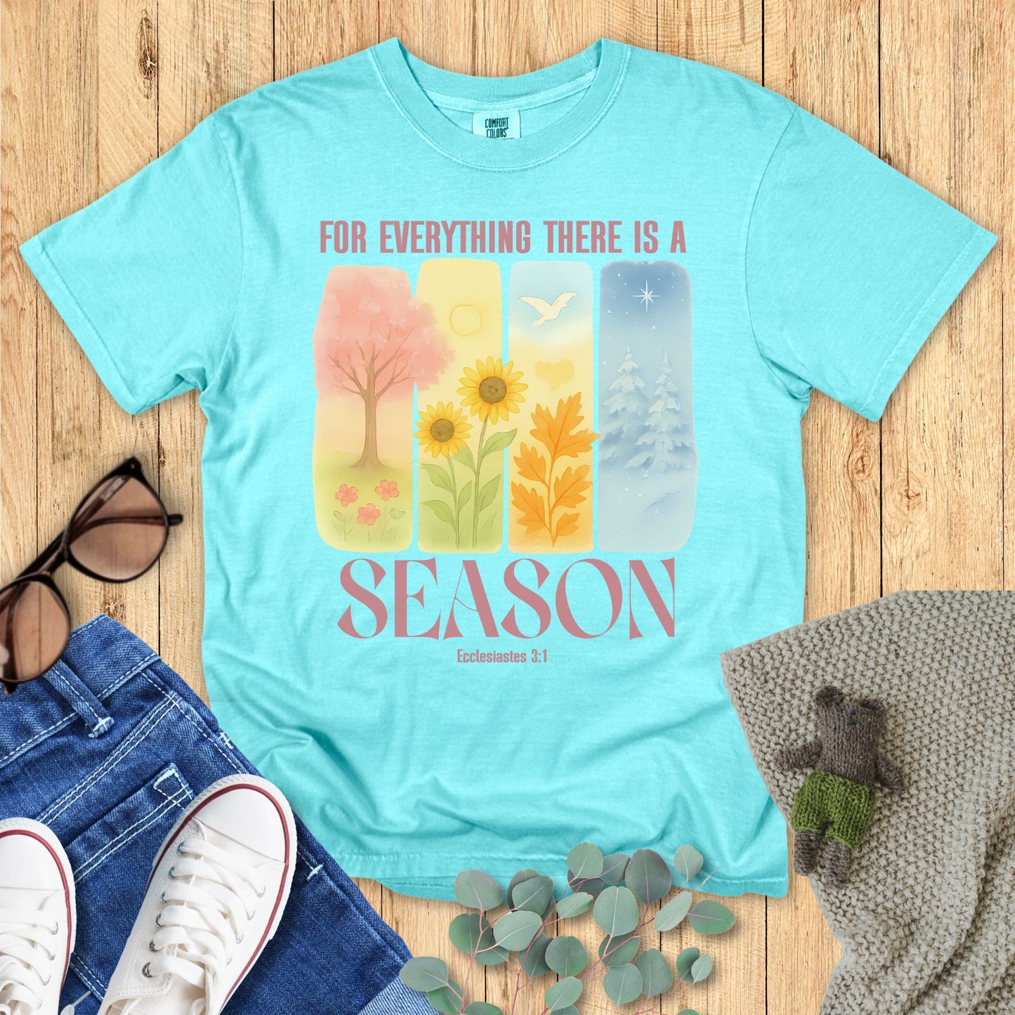 Light blue t-shirt with nature-themed design and text on a wooden surface with accessories.