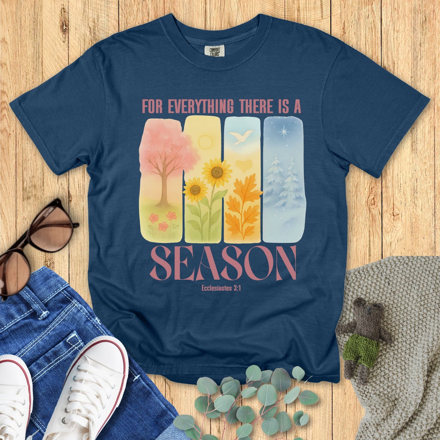 Blue t-shirt with 'For Everything There is a Season' design on a wooden surface with accessories.