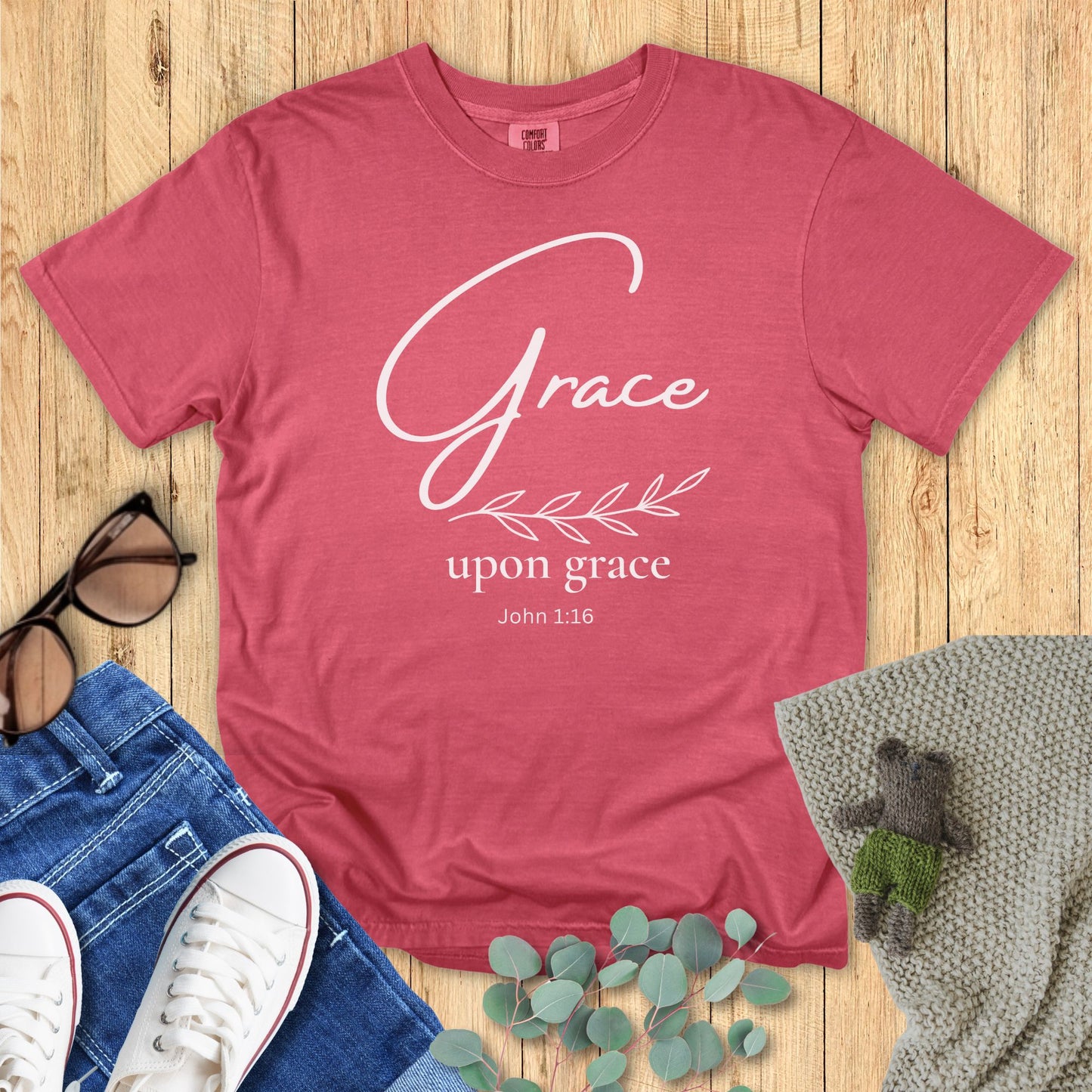 Crimson Red t-shirt with 'Grace upon grace John 1:16' text on a wooden surface with accessories.